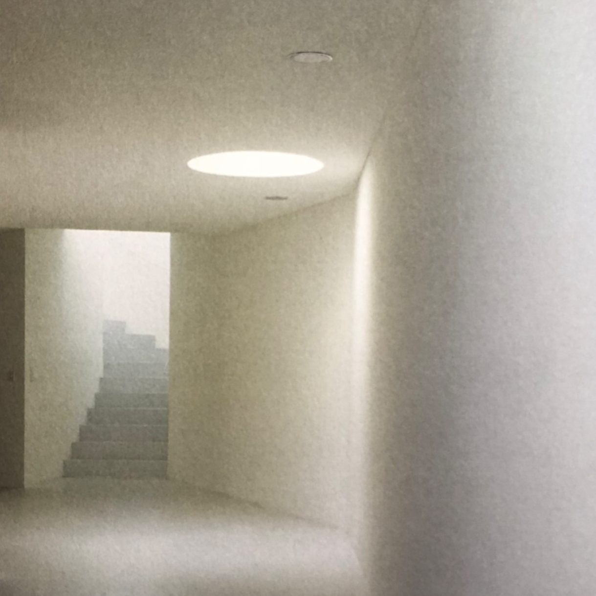 A staircase with a curved wall leading up, illuminated by a round ceiling light in an all-white interior.