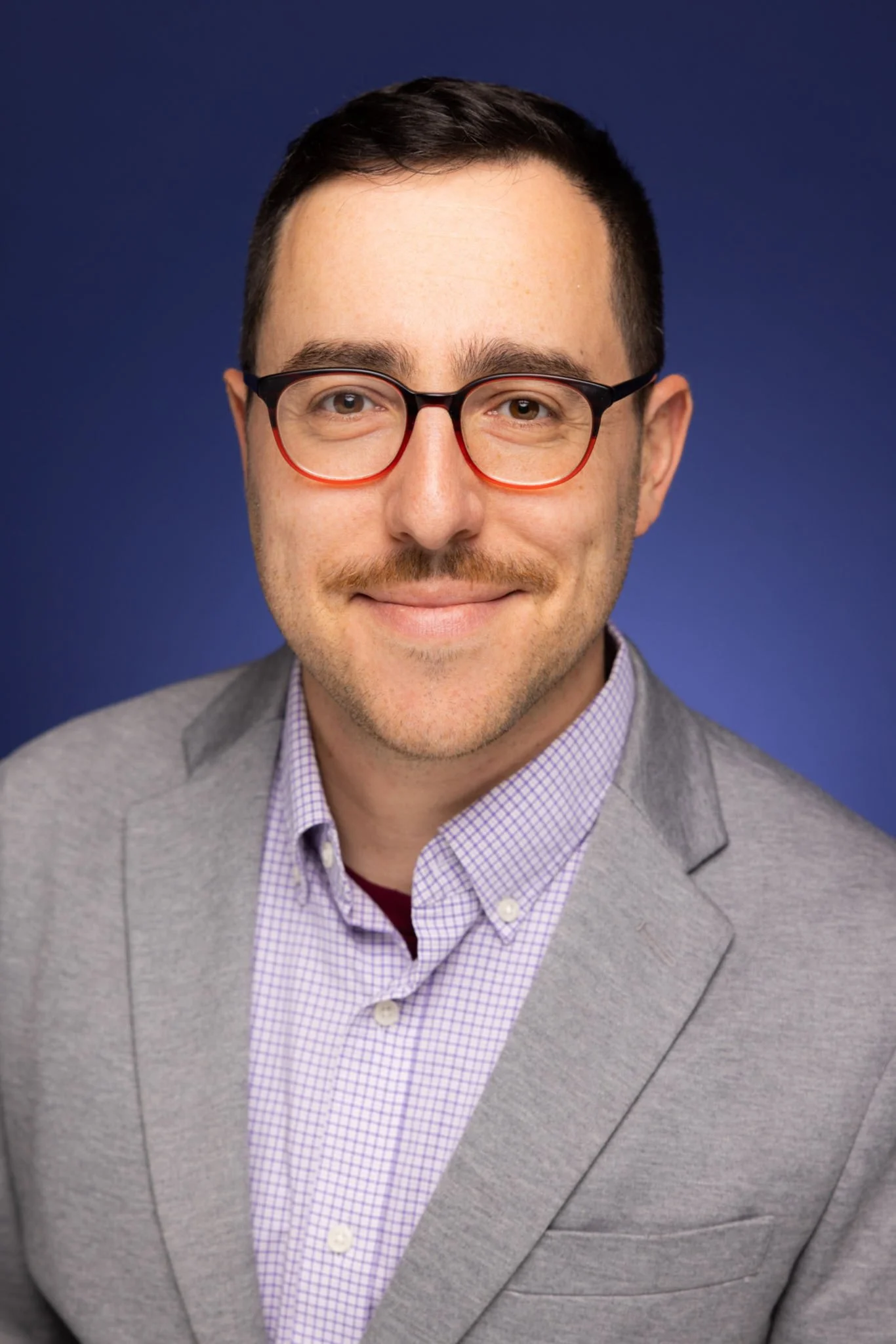 A male chef wearing a white chef's hat and jacket, standing in an indoor setting with decorative wall background.