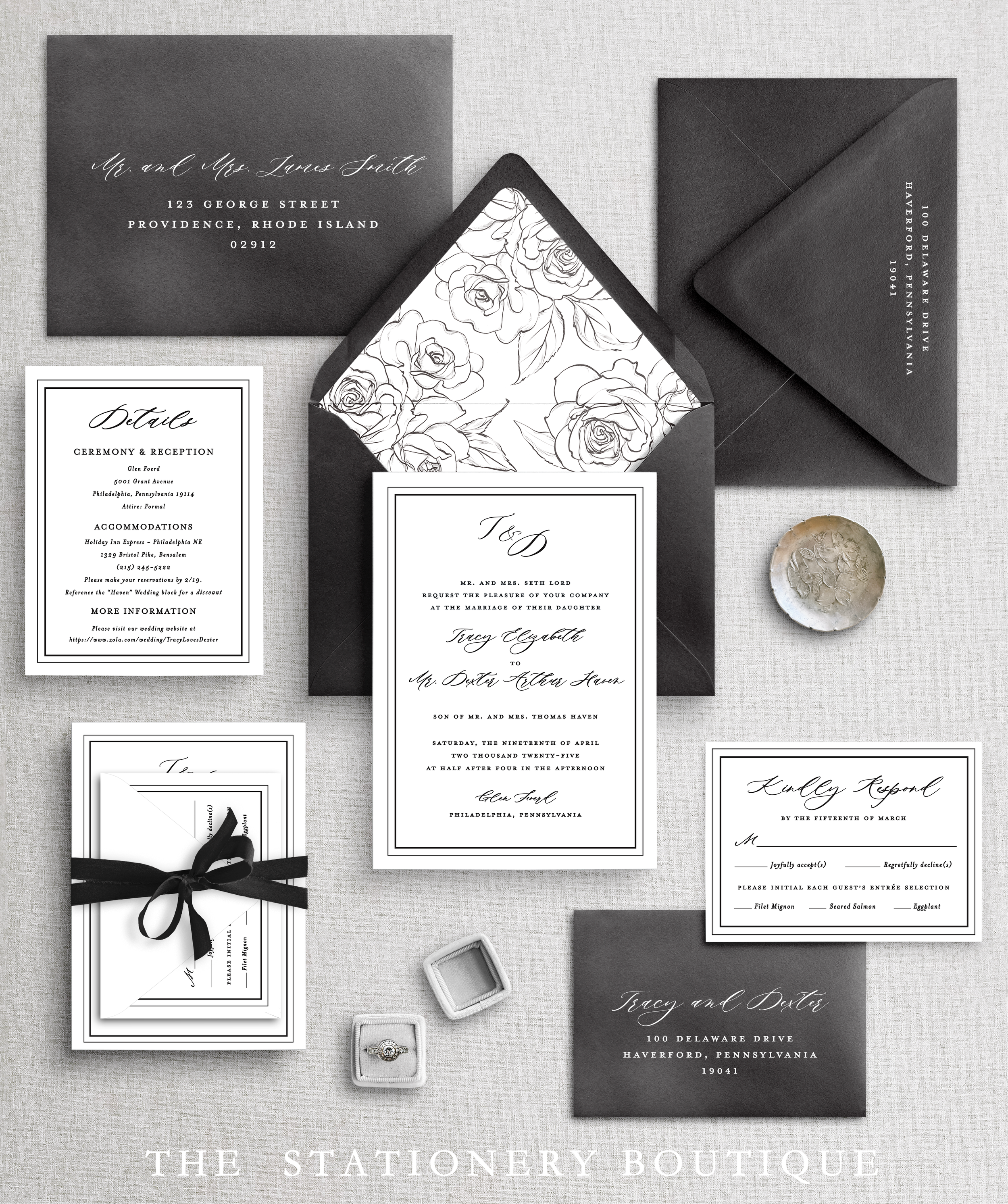 Elegant black and white wedding stationery includes invitations, RSVP card, information card, envelope with floral interior lining, and black envelopes, along with a small ring box and a ring, displayed on a gray textured surface.
