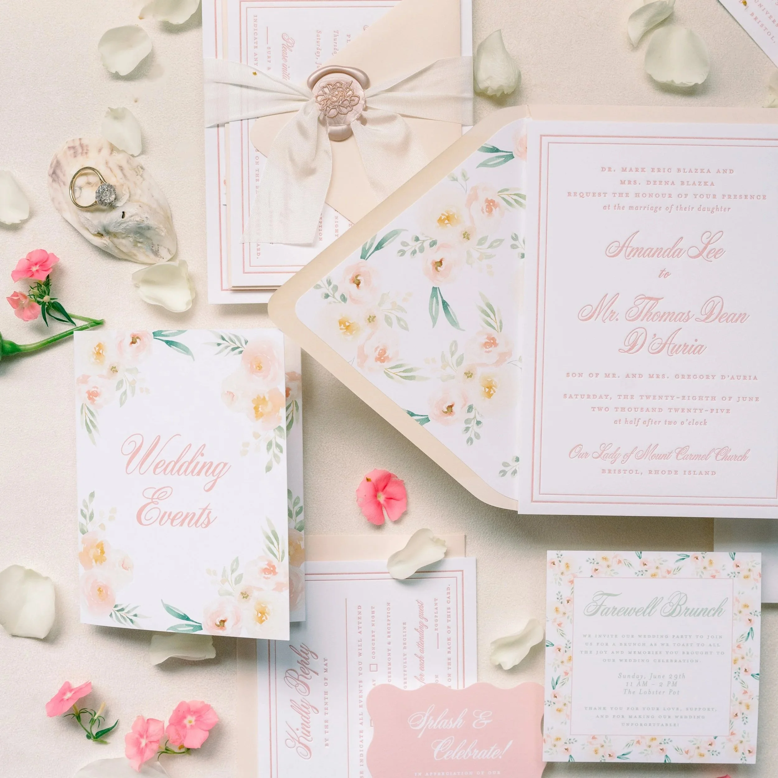 Wedding invitation suite with floral motifs, RSVP card, and event details, surrounded by flower petals, a shell with a ring, a sealed envelope, and a pink flower, all set on a white surface.