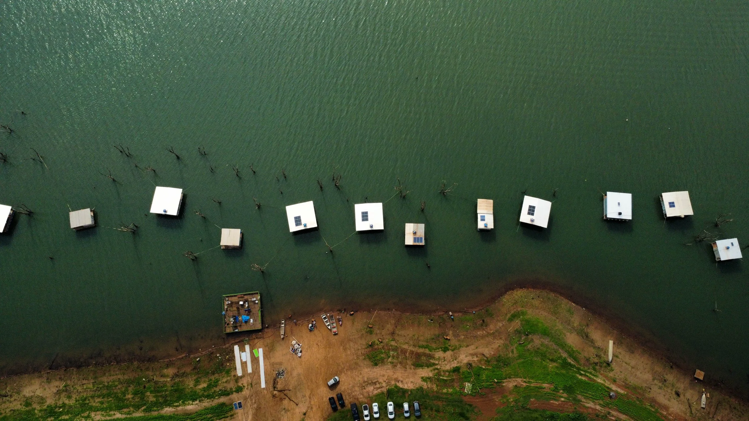 Vista aérea do Mata dos Macacos em Guaraci (SP), com batelões de pesca flutuantes no Rio Grande e área de acesso na margem.