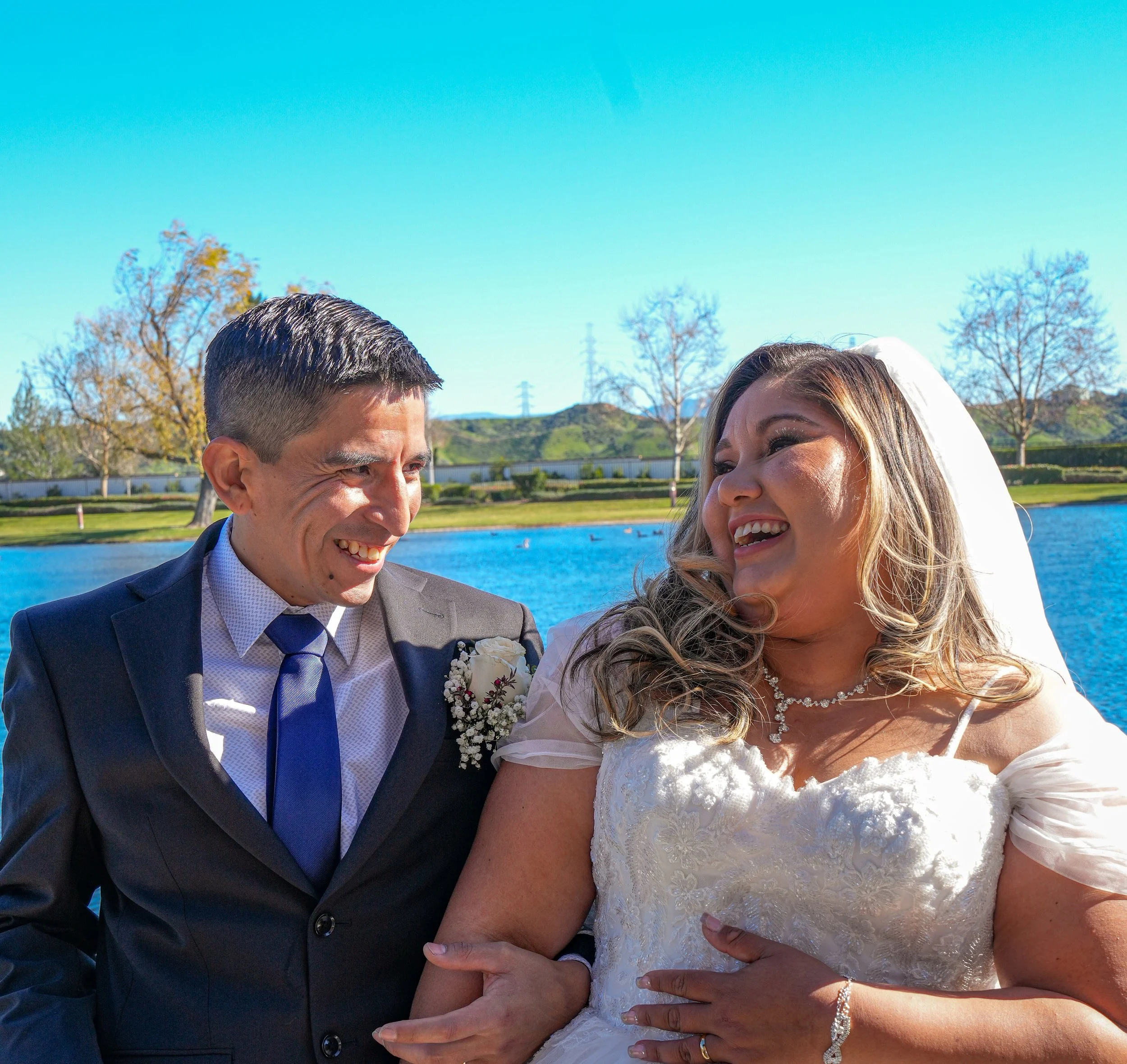 Happy bride and groom smiling together outdoors by the water on their wedding day.