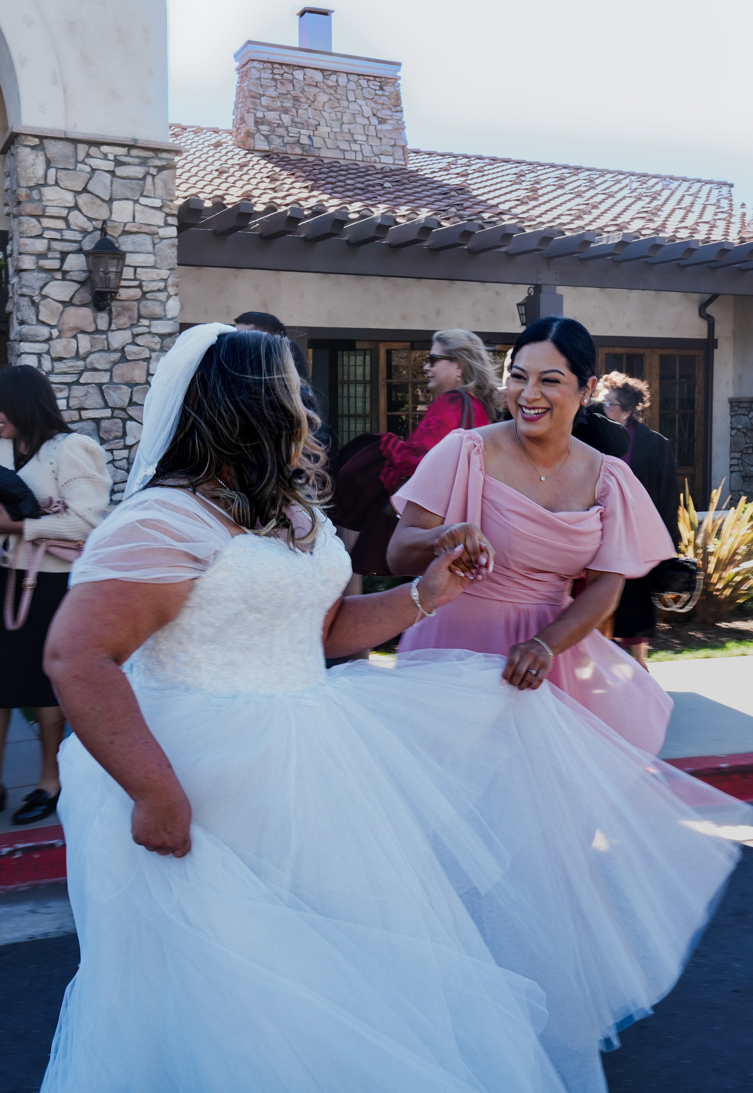 Women dancing at a wedding reception outside a house with stone exterior and tile roof.