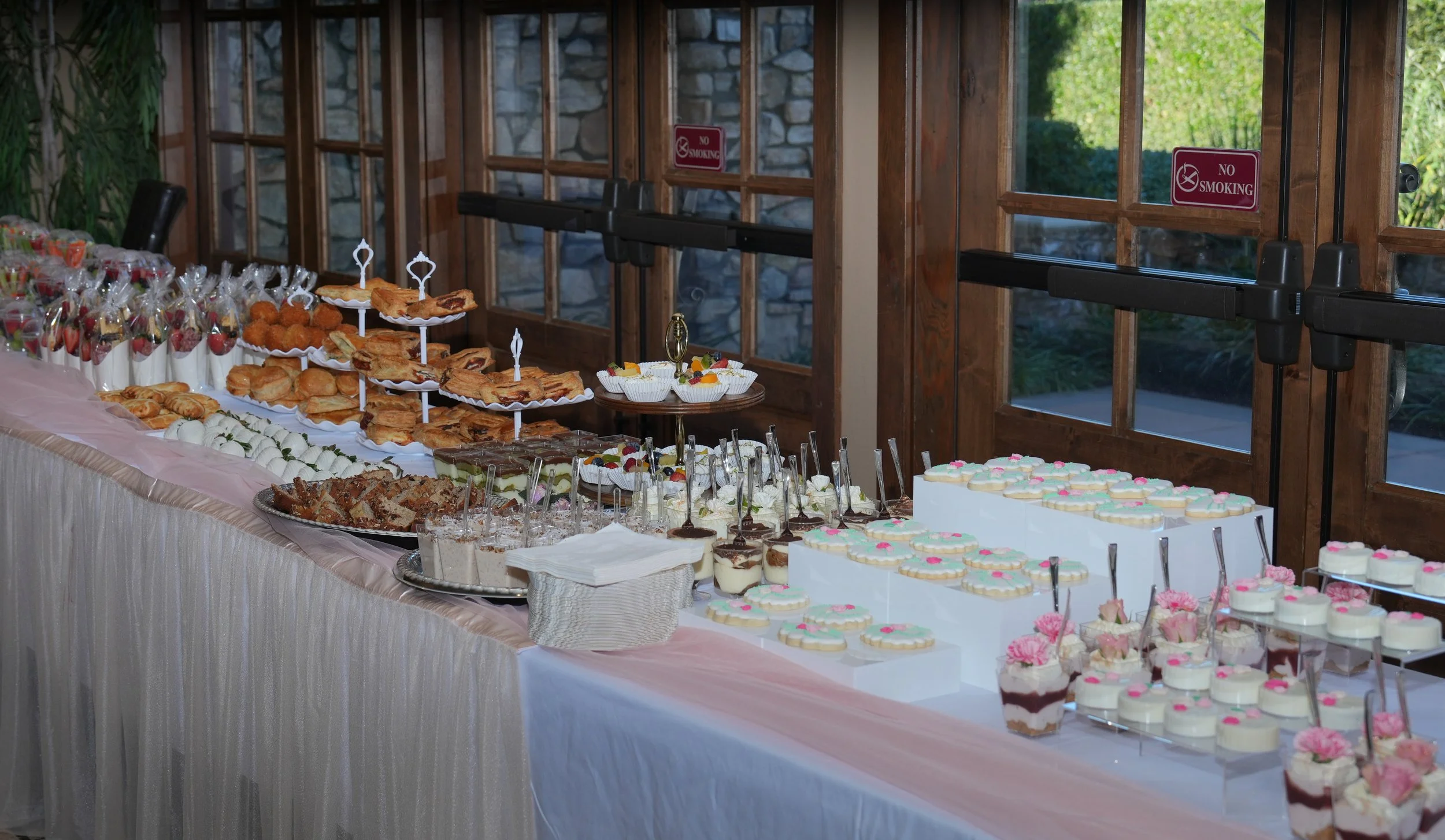 Dessert table with cakes, cupcakes, cookies, and other sweet treats in a decorated banquet hall.