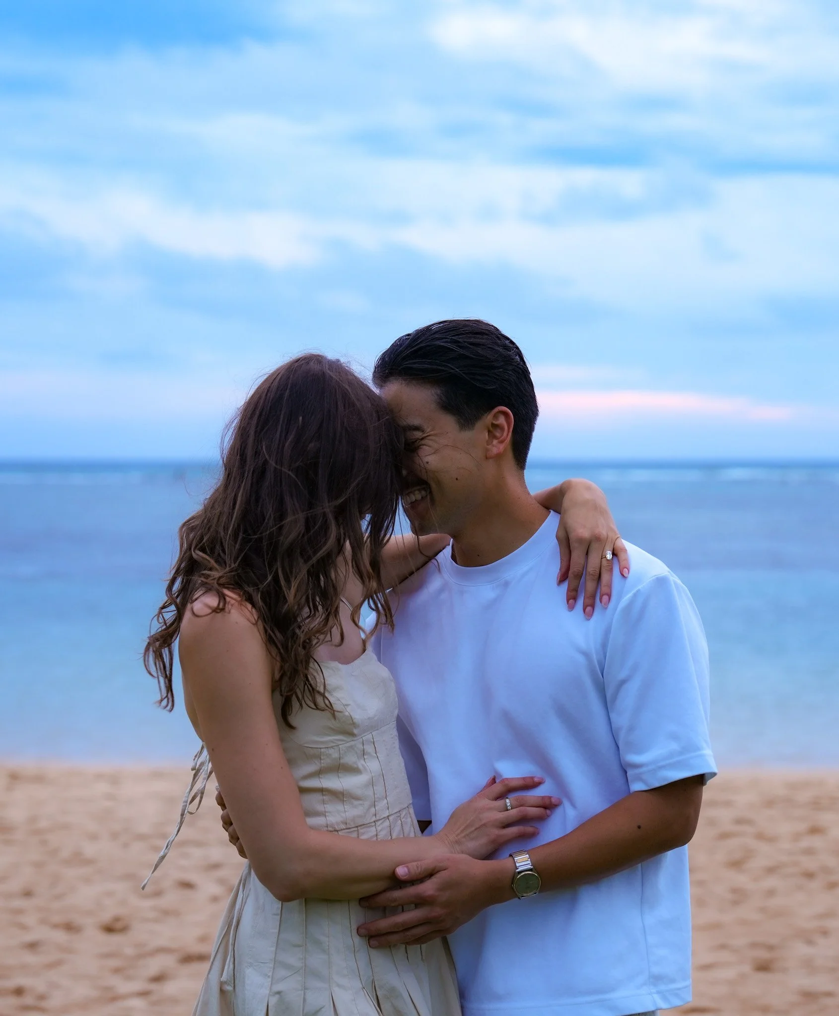 A couple hugging and smiling on a beach at sunset.