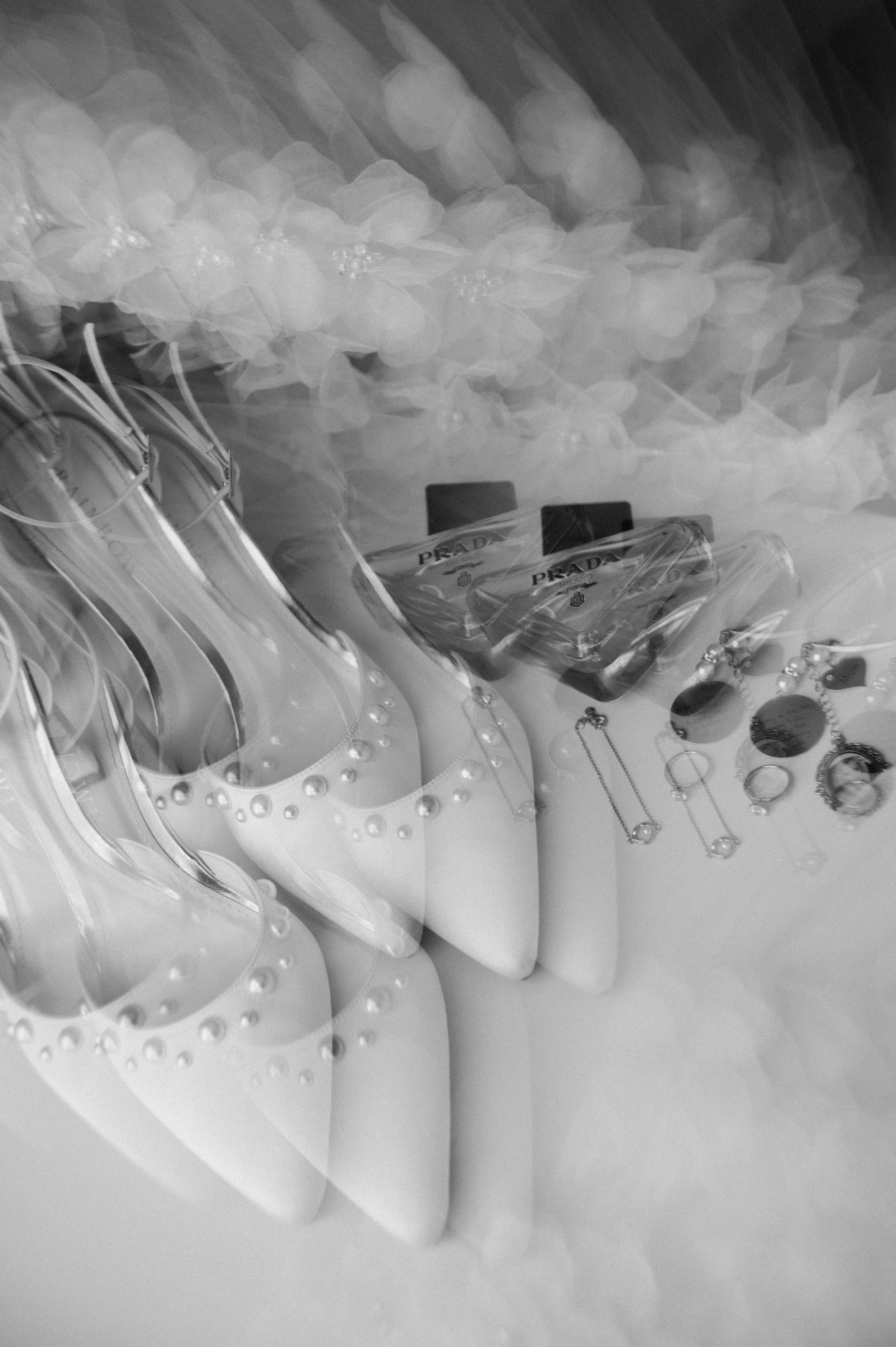 Display of designer accessories including white high-heeled shoes with pearls, multiple pairs of earrings, necklaces, and Prada perfume bottles.