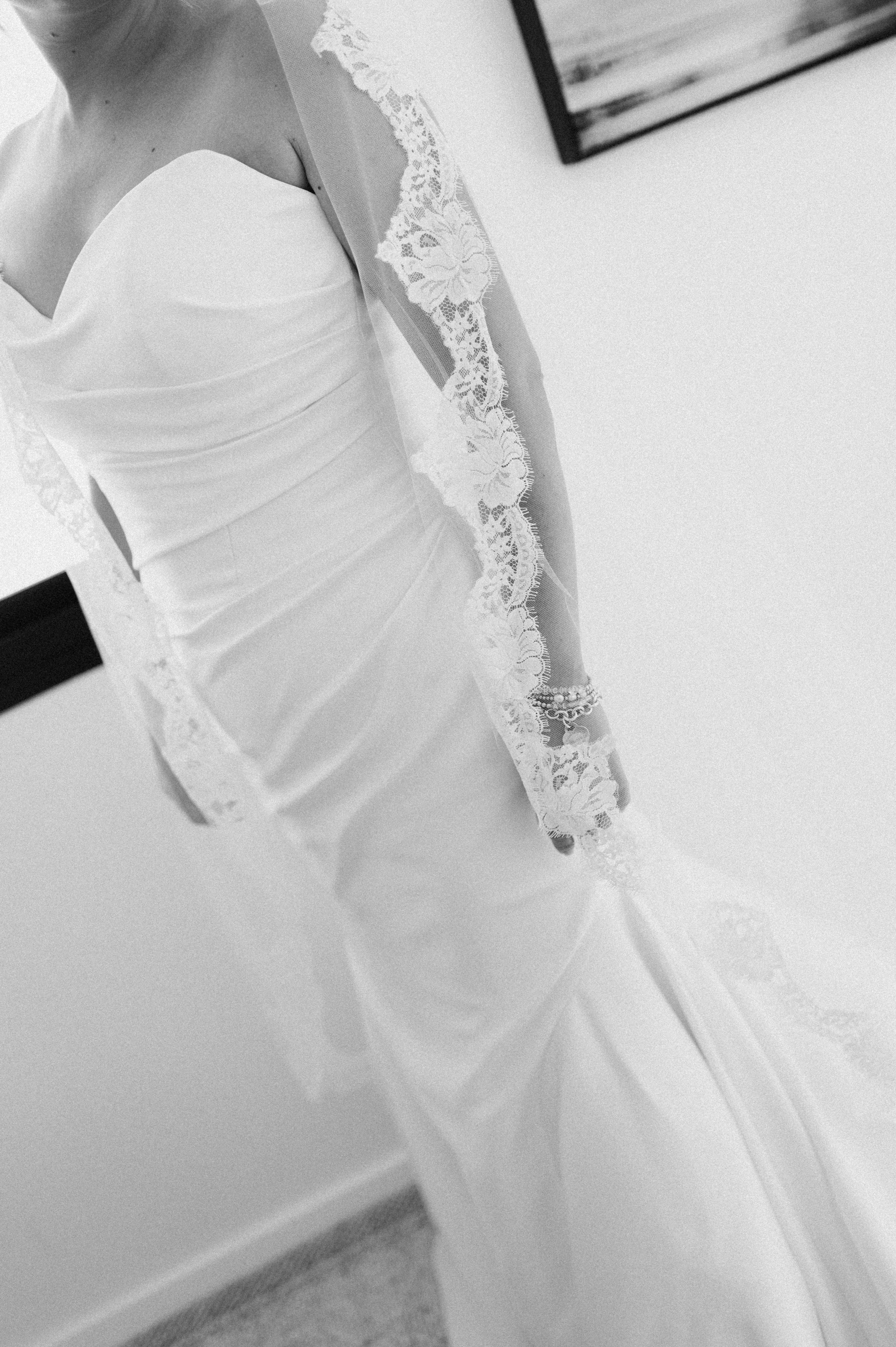Close-up of a woman wearing a white wedding dress with lace details on the sleeves and a fitted satin bodice.