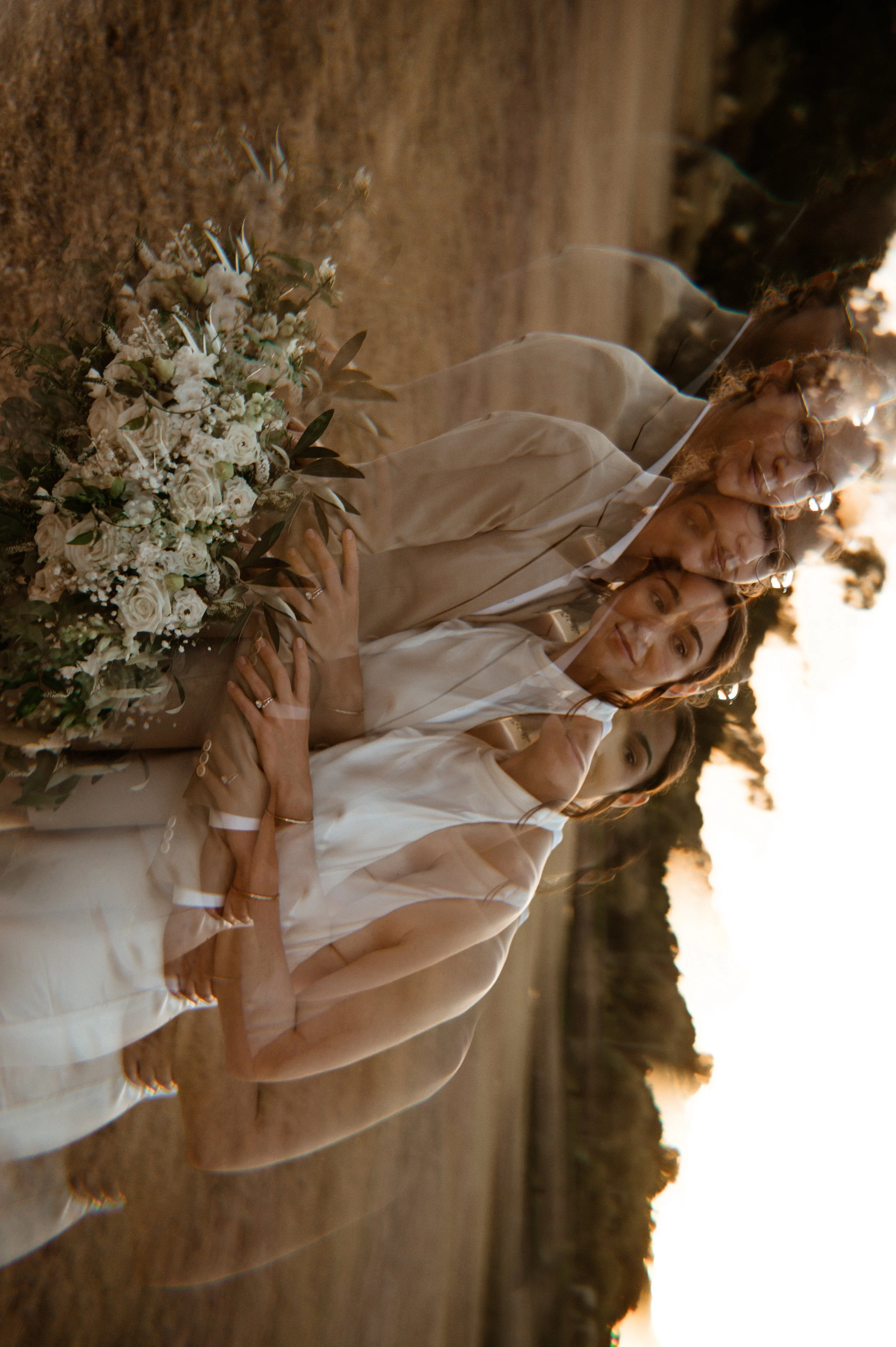A layered image of a bride and three women in white dresses, with a large bouquet of white flowers on the ground in an outdoor setting during sunset.