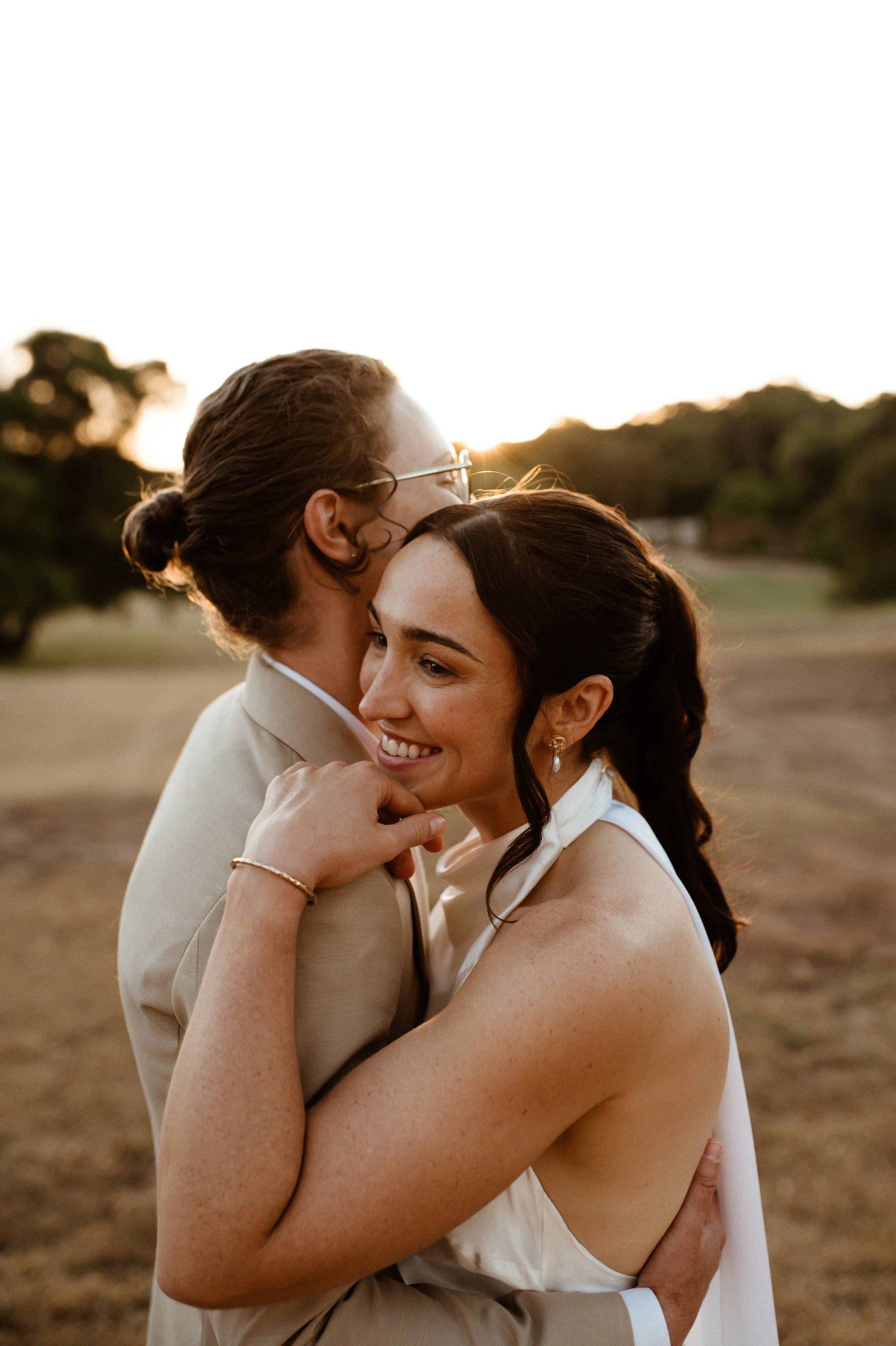 A happy couple embracing outdoors during sunset, with trees and open field in the background.