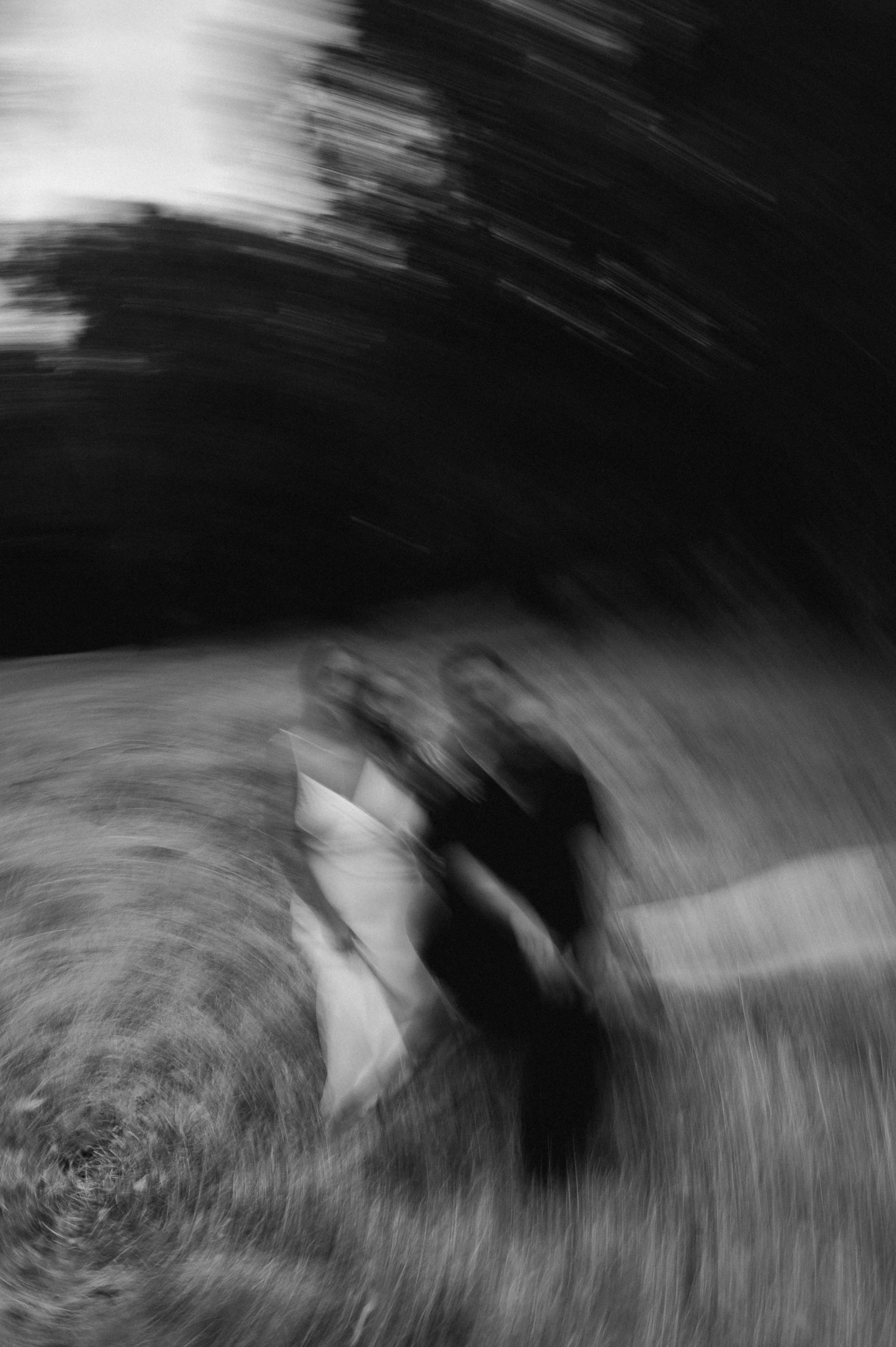 Two people standing on grass with trees in the background, captured with a blurred, spinning effect in black and white.