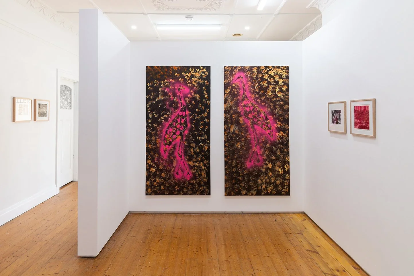 Two painted artworks on a gallery wall in golds, browns and neon pink