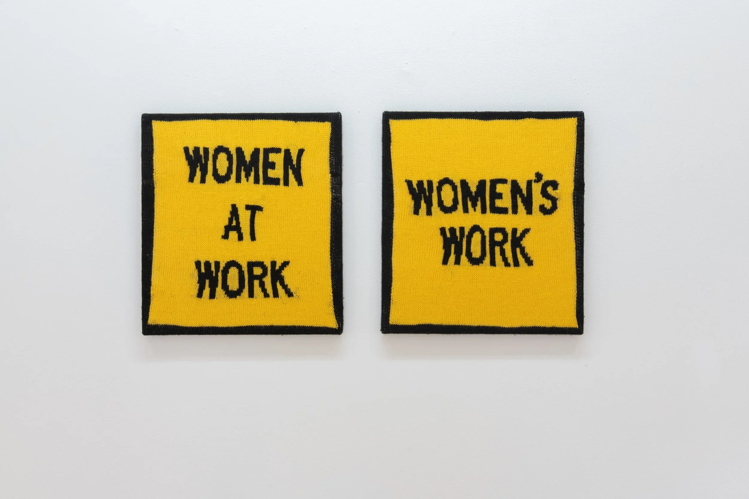 Two knitted artworks on gallery wall reading 'Women at Work' and 'Women's Work'