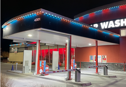 A modern gas station with fuel pumps under a roof decorated with colorful lights at night.