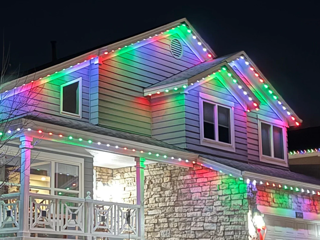A two-story house decorated with colorful Christmas lights at night.