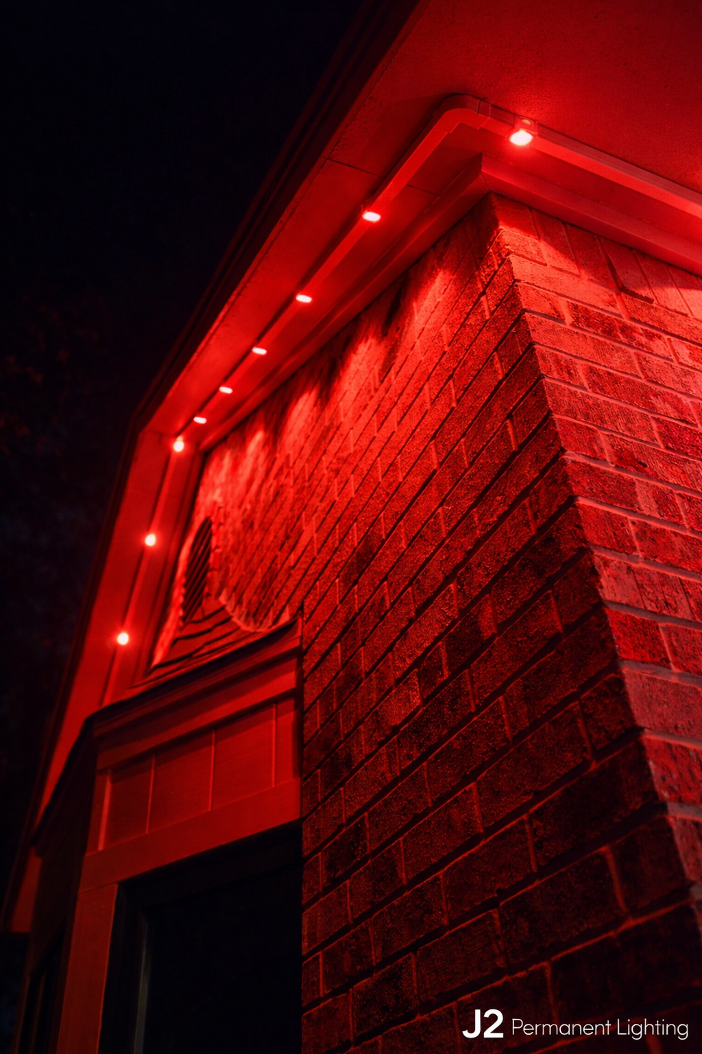 Close-up of a brick chimney with red outdoor Christmas lights illuminating it at night.