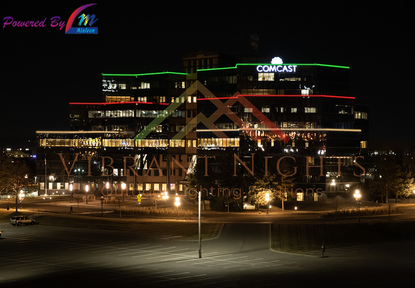 Nighttime cityscape with illuminated buildings, including a Comcast building with green and white lighting, and a neon sign reading 'Vibrant Nights' in the foreground.