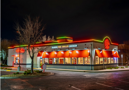 Famous Fire-Grilled Chicken restaurant building with neon signs and red awnings at night.