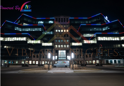 Night view of a modern multi-story building with colorful neon lights and the signs 'Powered By M' and 'VIBRA LIGHTS'.