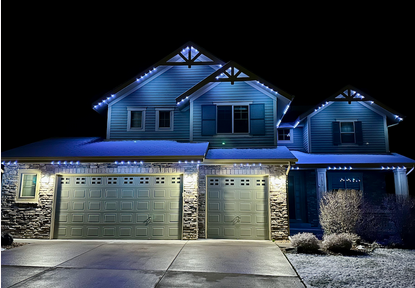 A two-story house with a stone facade, three garage doors, and blue exterior lighting at night.