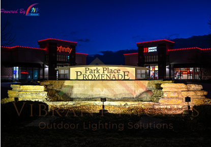 Night view of Park Place Promenade shopping center with illuminated signs and water feature in foreground.