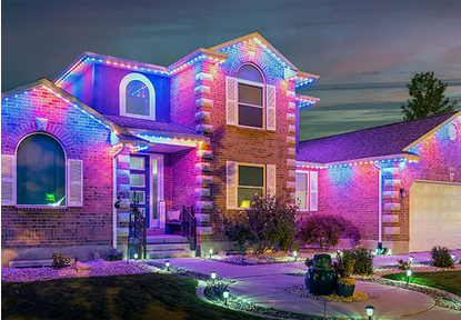 A two-story brick house decorated with colorful Christmas lights, including pink, purple, and blue, outlining the roof, windows, and entrance area, with a landscaped front yard at dusk.