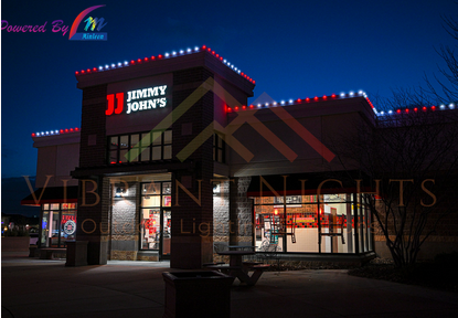Jimmy John's restaurant illuminated at night with colorful string lights and bright signage.