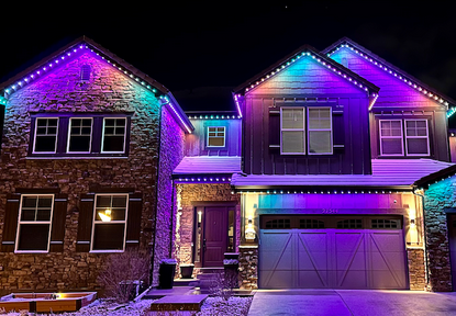 A two-story house decorated with colorful Christmas lights at night.
