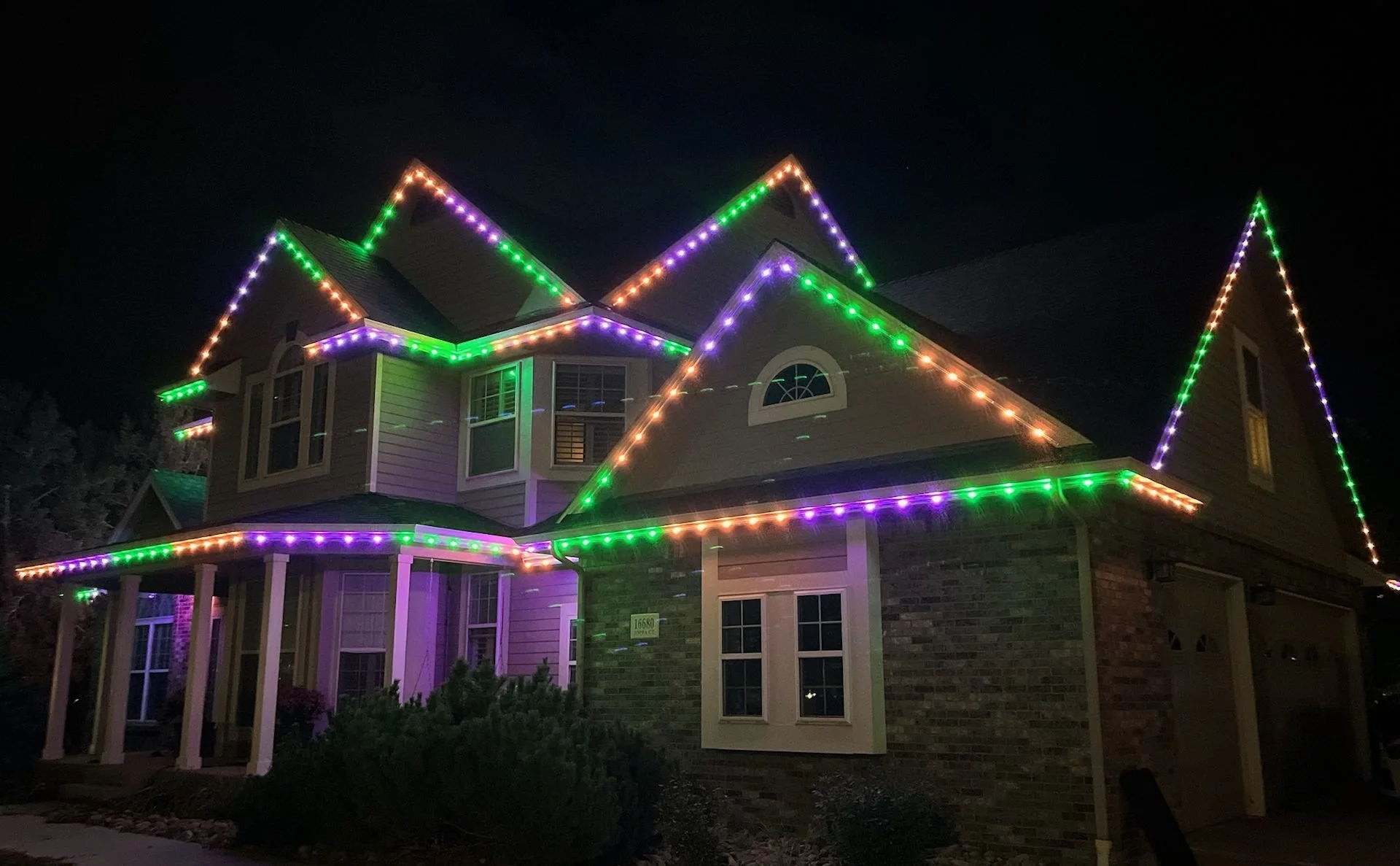 A two-story house decorated with multicolored Christmas lights along the rooflines at night.
