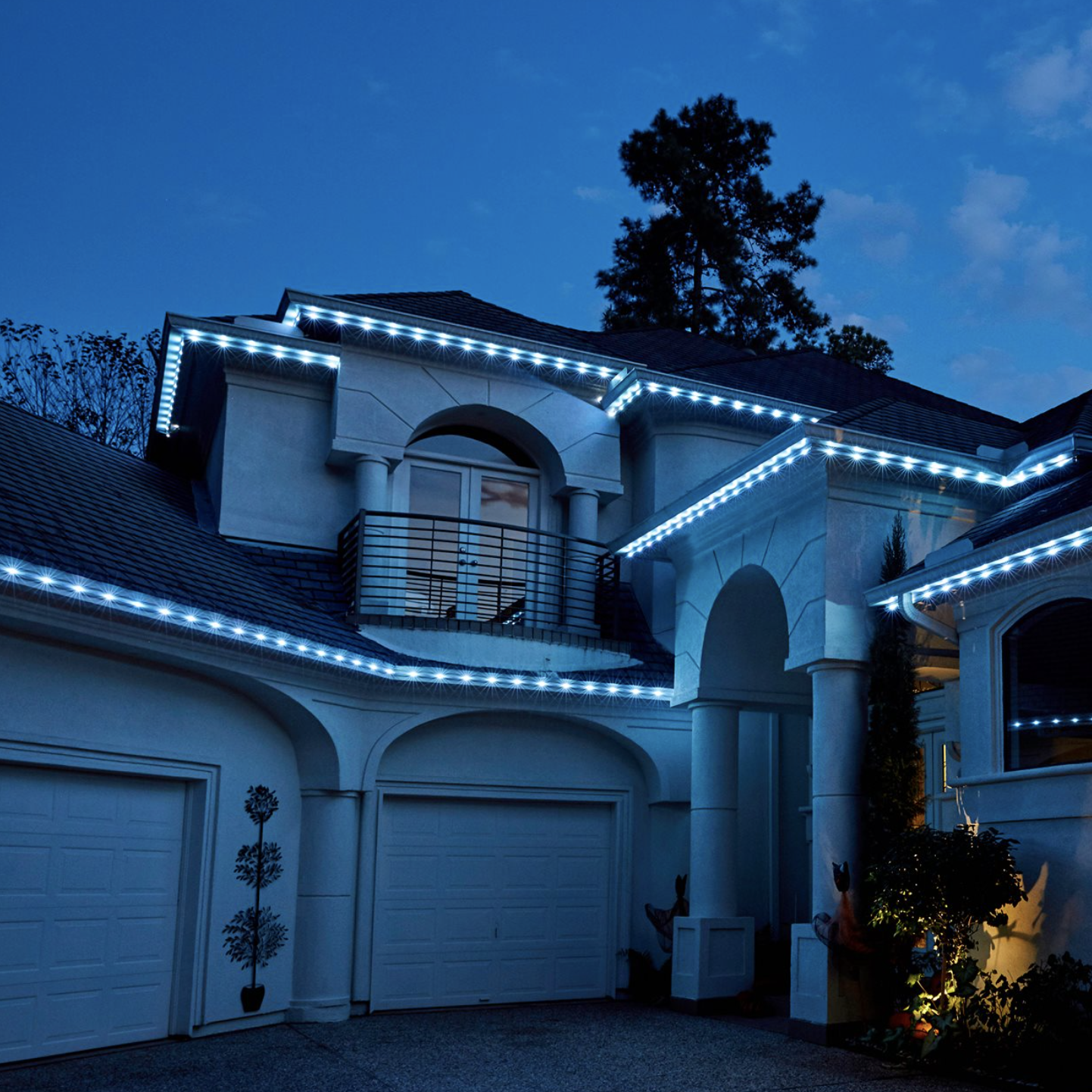 A large house decorated with white Christmas or holiday lights outlining the roofline and edges at dusk.
