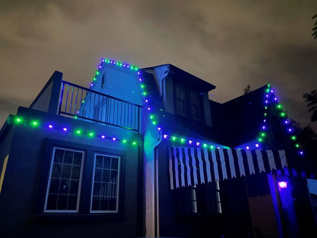 House decorated with multicolored Christmas lights at night with an awning and windows.