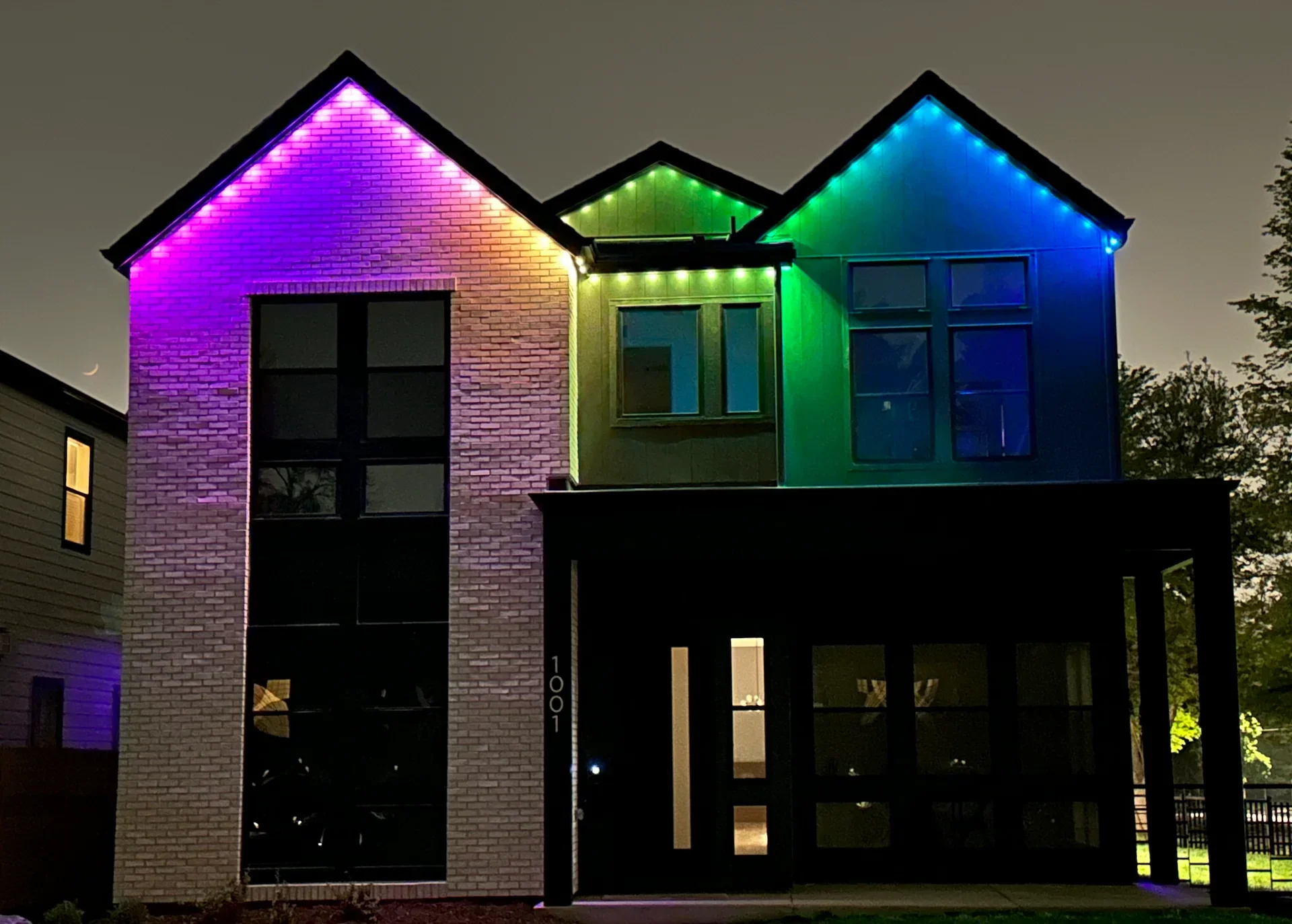 Night view of a modern house illuminated with colorful LED lights in purple, green, and blue.