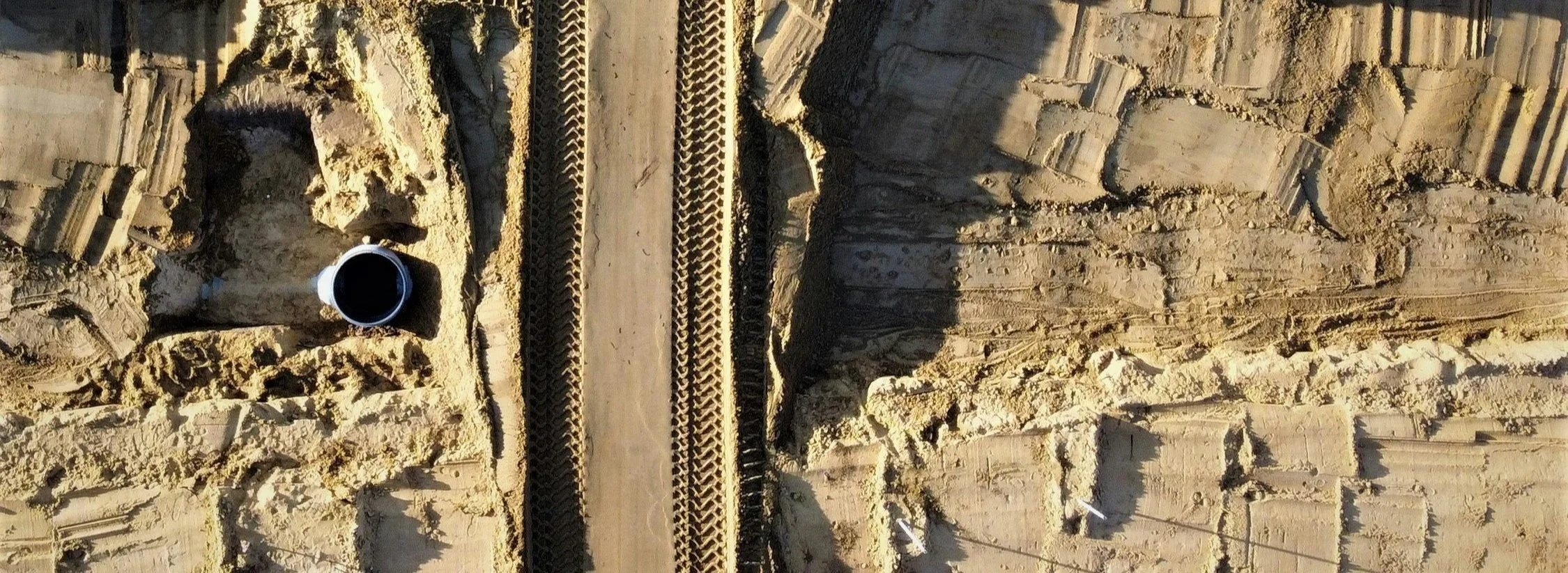 View of a construction site showing manhole connection and pipe, surrounding dirt, and a black pipe protruding from the ground.