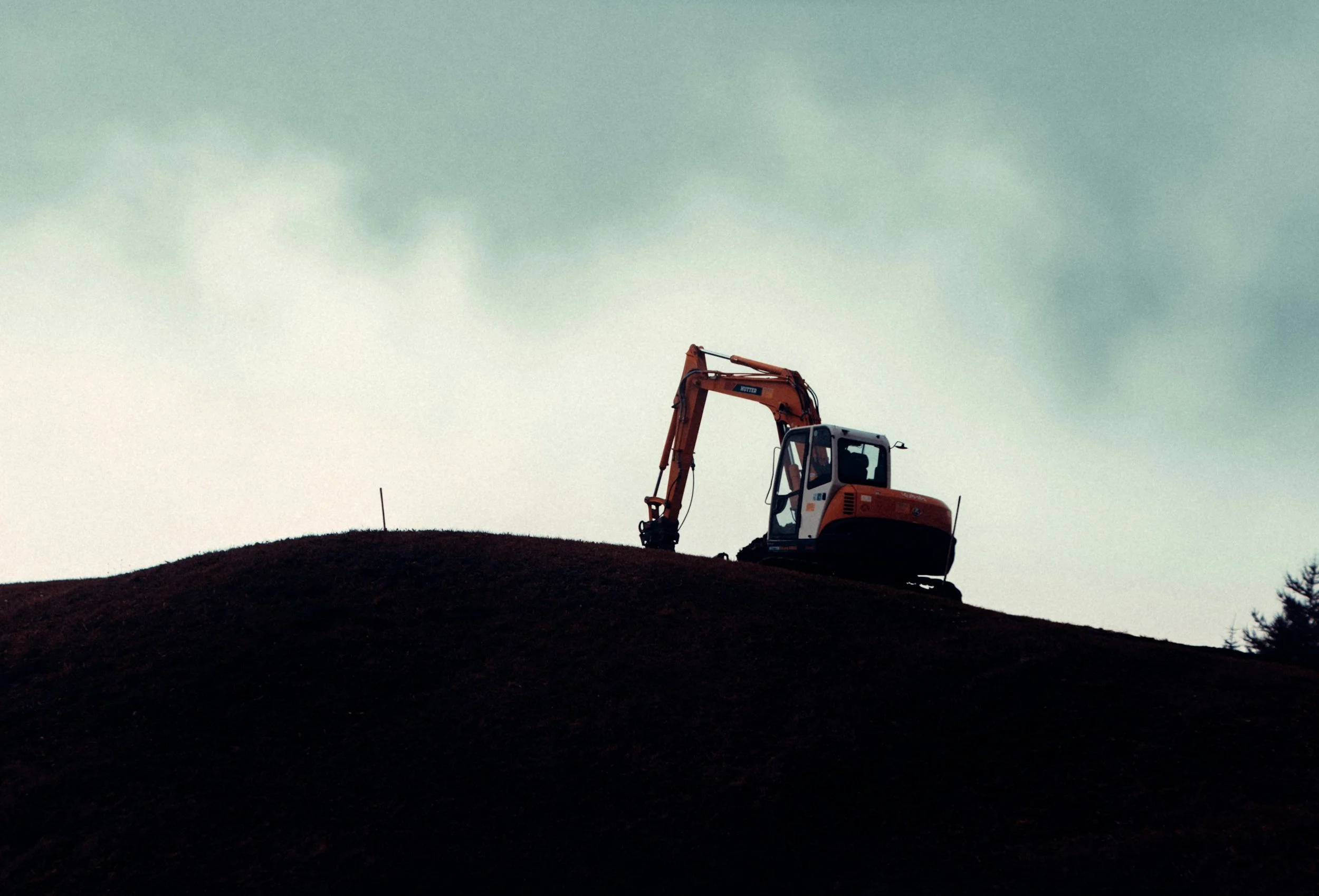 Silhouette of an excavator on a hill against a cloudy sky during daytime.