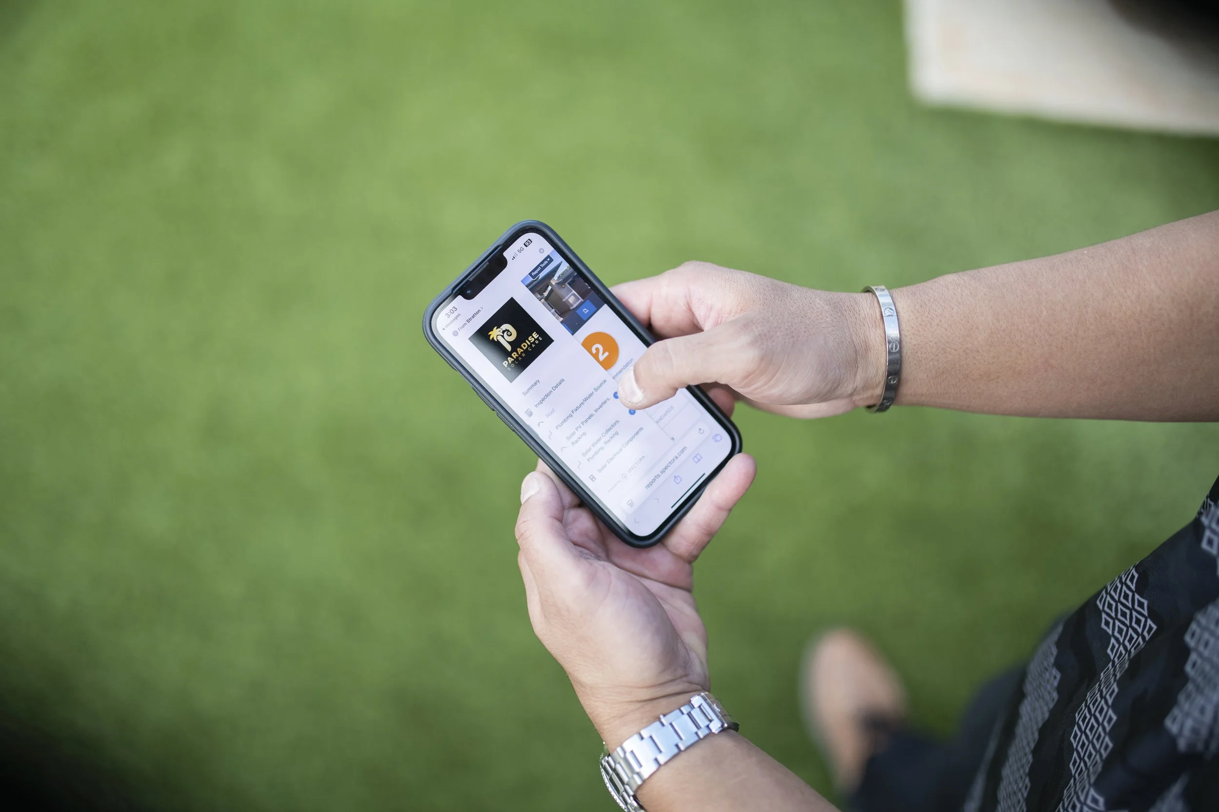 A person holding a smartphone, looking at a webpage on the screen with a green outdoor background.