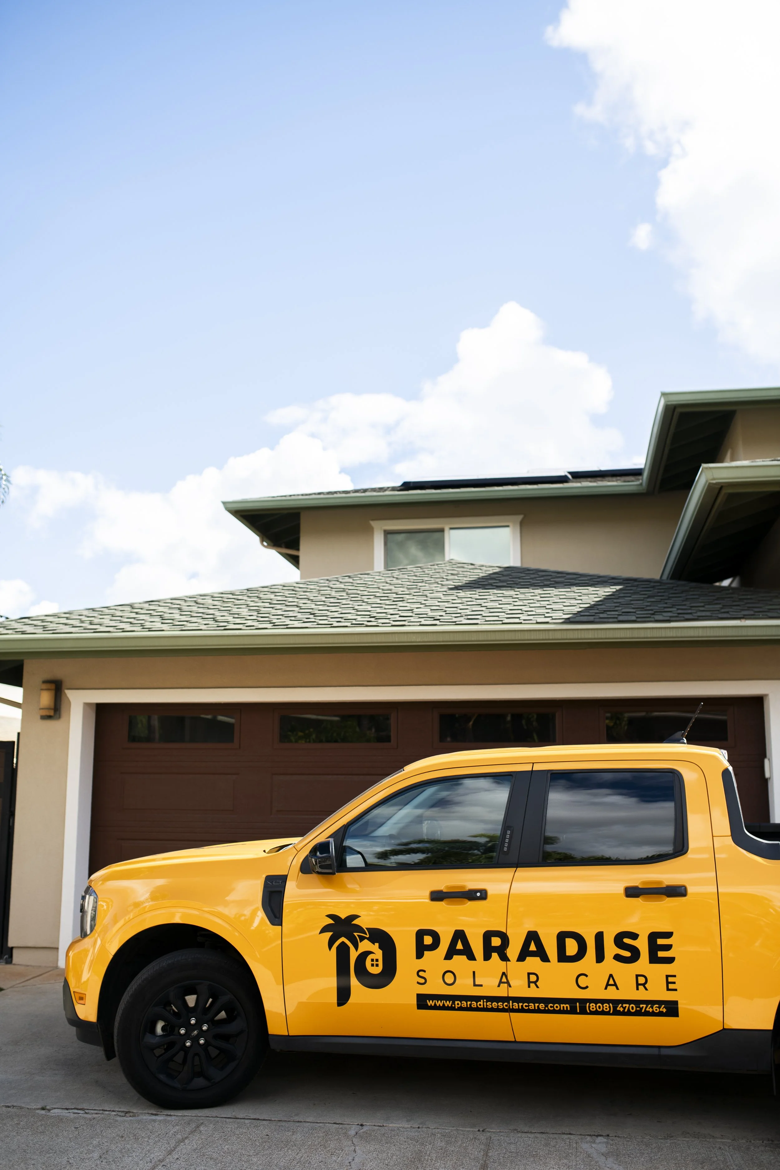 Yellow Paradise Solar Care vehicle parked in front of a modern house with a garage, under a partly cloudy sky.
