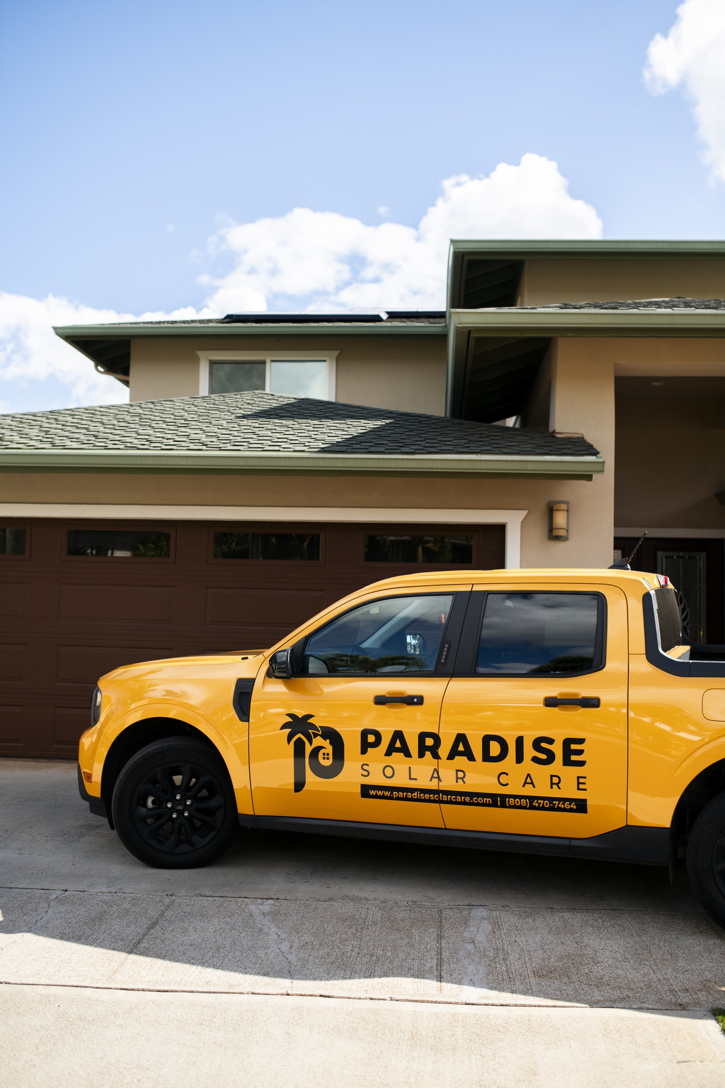 Yellow Paradise Solar Care company vehicle parked in front of a residential house with a brown garage door and beige exterior walls.
