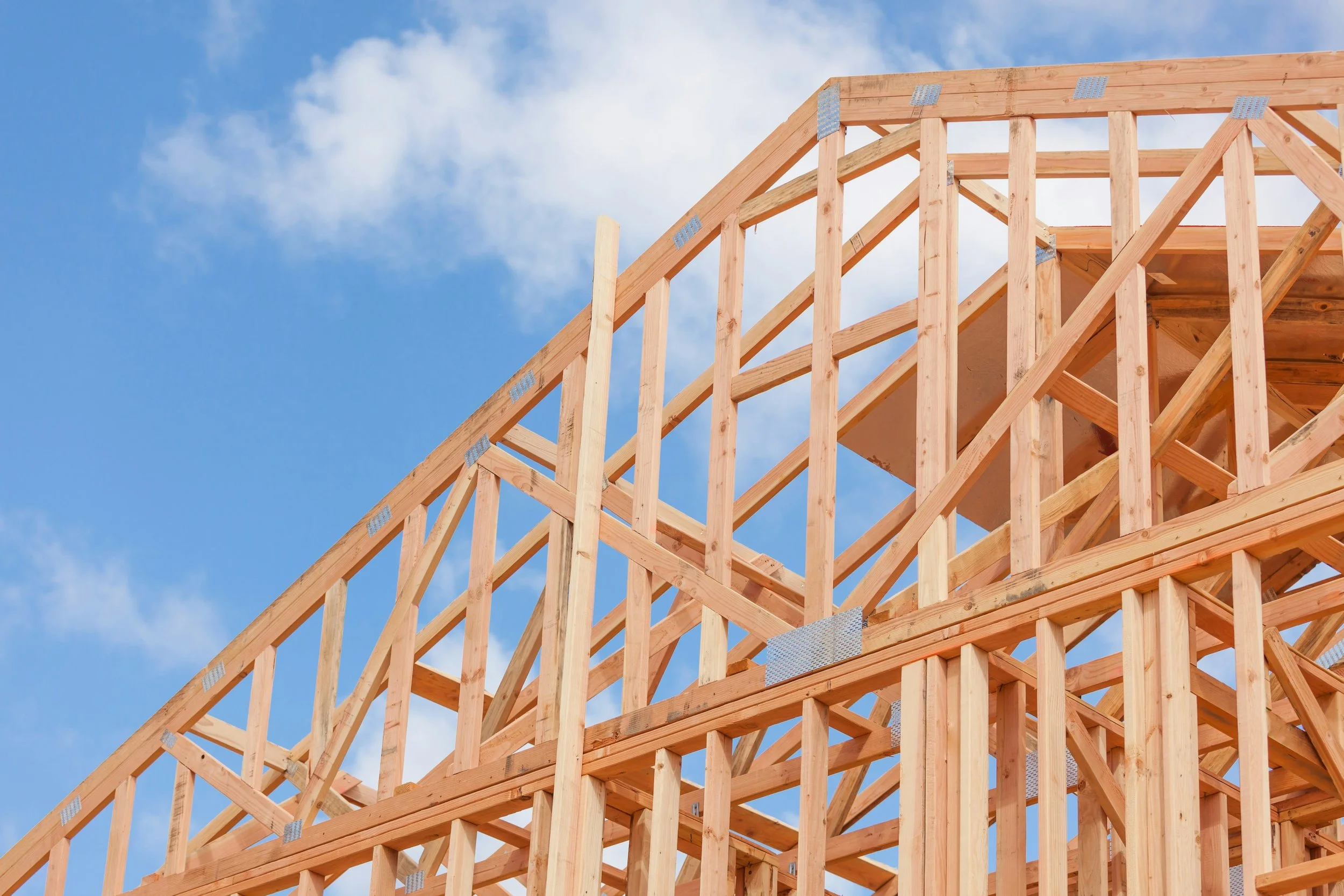 Wooden framing of a building under construction against a blue sky with clouds.