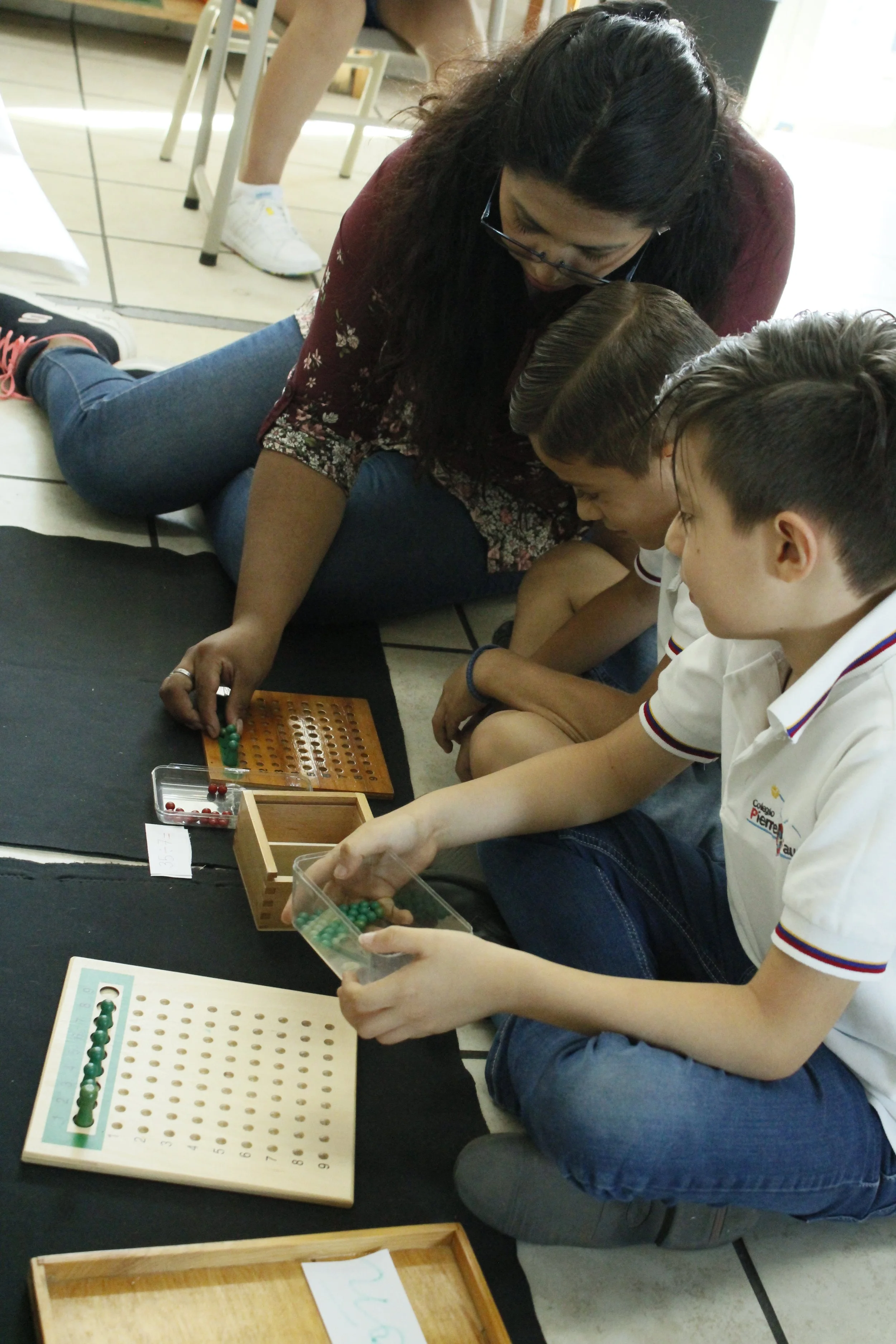 Una mujer y dos niños jugando a un juego de mesa en un suelo de baldosas blancas y negras.