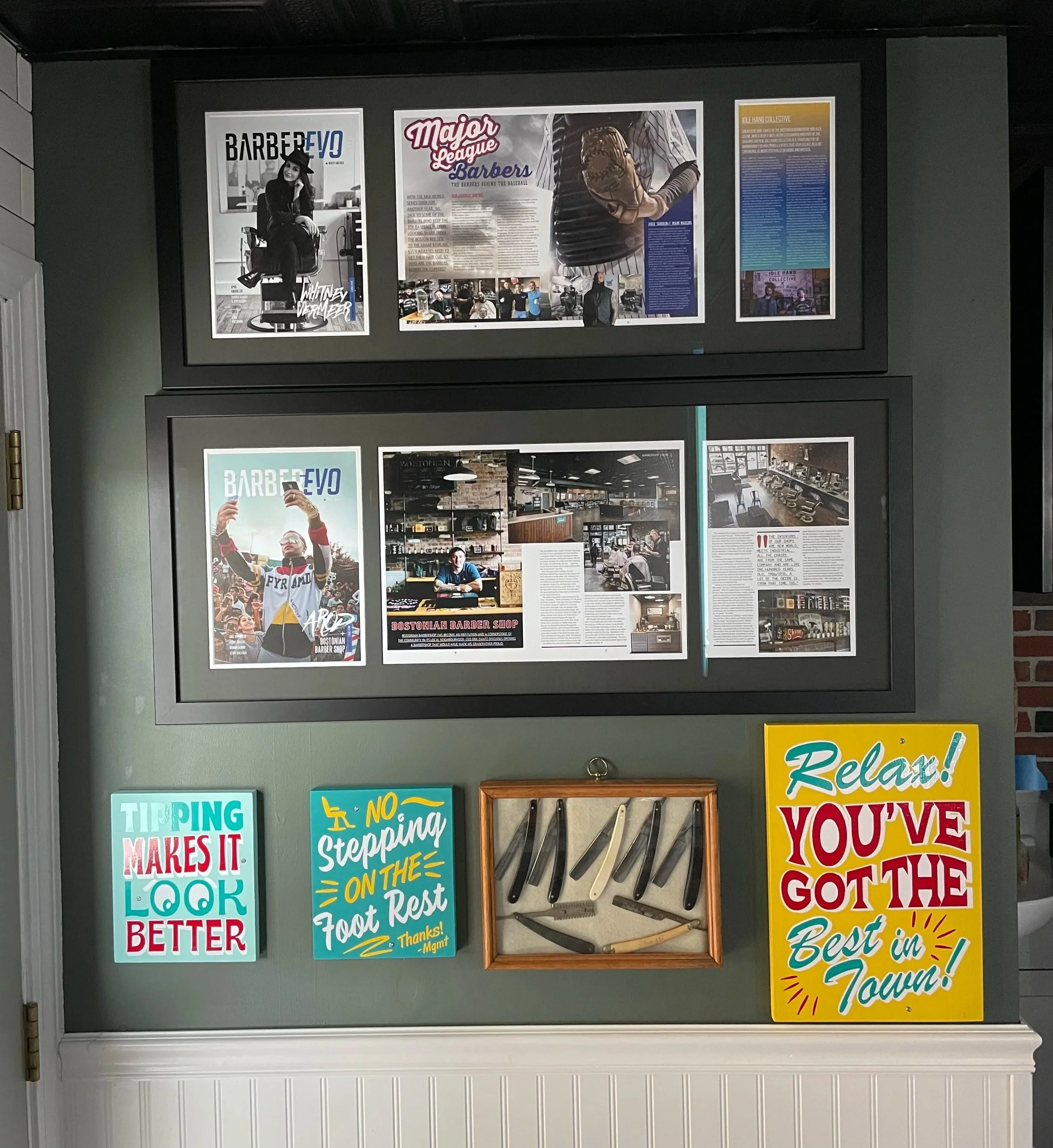 Display of framed photos and articles about a barbershop, along with colorful motivational signs and a knife collection on a wall.
