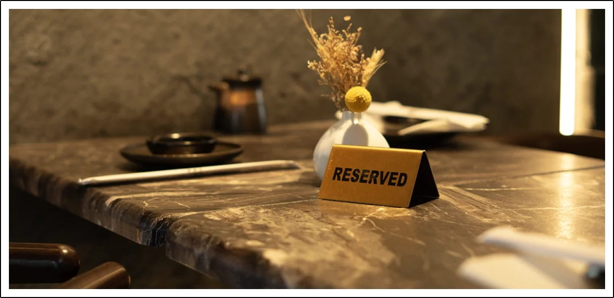A reserved table in a restaurant with a marble top, decorated with a white vase and dried flowers, and a reserved sign.