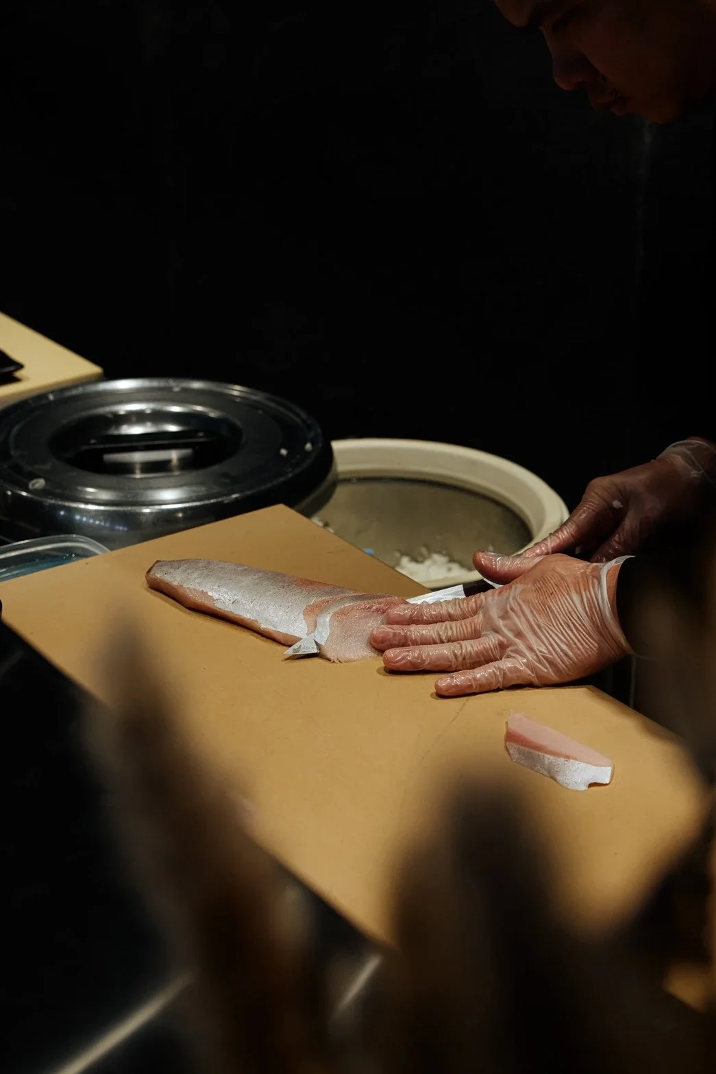 Person wearing gloves preparing a fish fillet on a cutting board in a kitchen or restaurant setting.