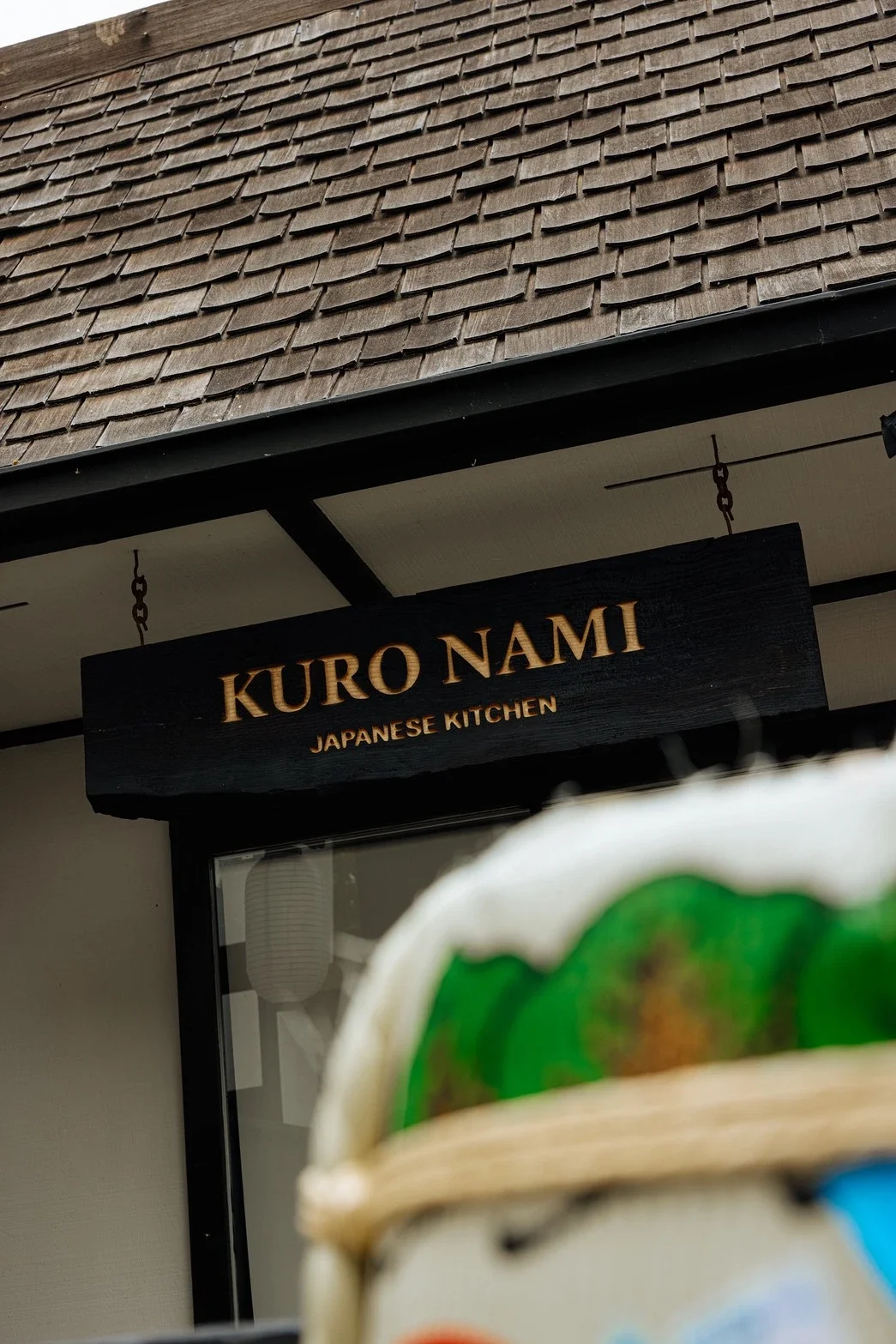 Sign for Kuro Nami Japanese Kitchen restaurant with a partial view of a sushi roll in the foreground.