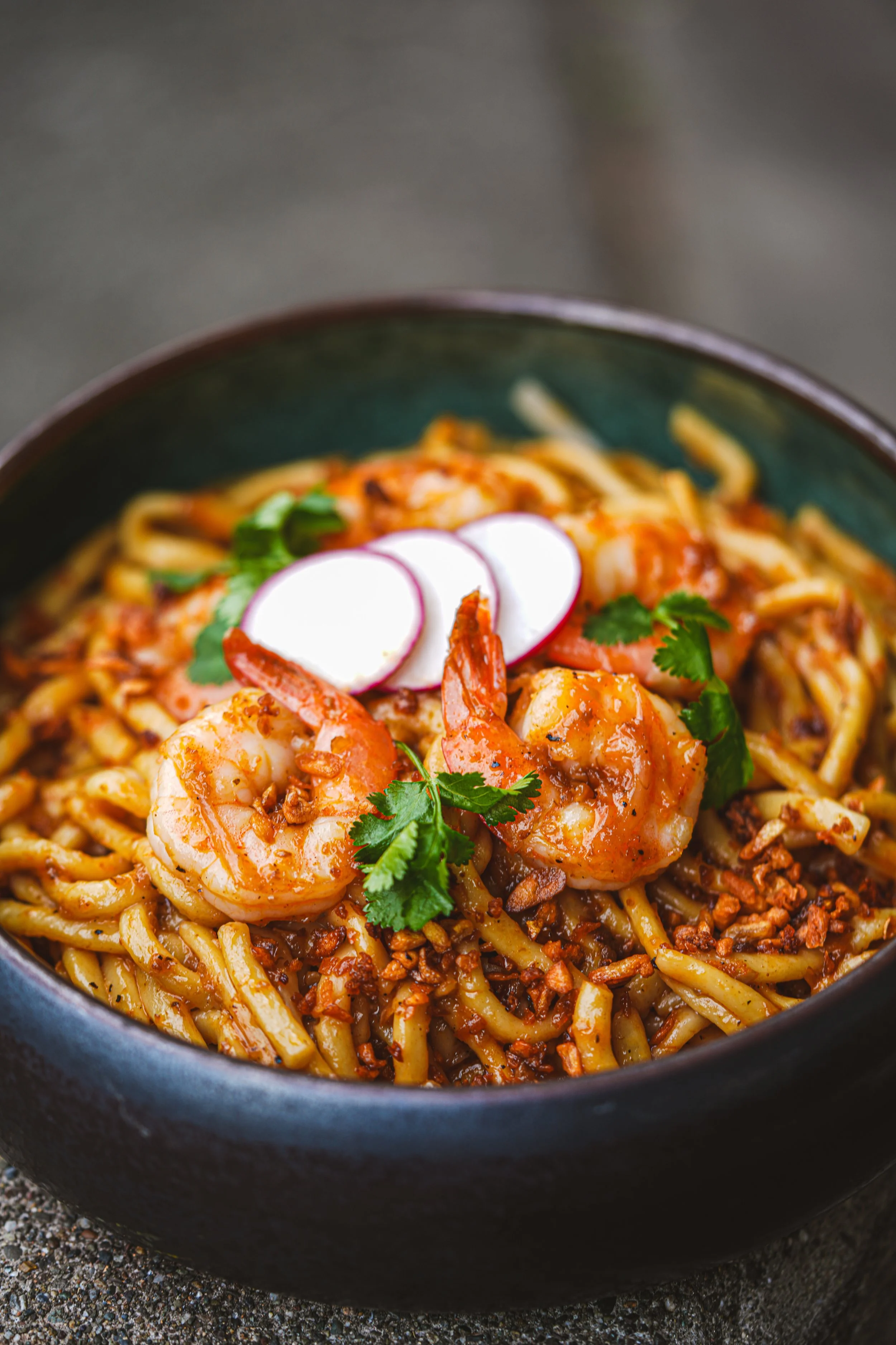 Close-up of a bowl of shrimp and noodle stir-fry garnished with sliced radishes and cilantro.
