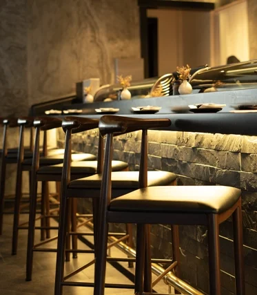 A restaurant bar counter with empty chairs, modern decor, and dim lighting.