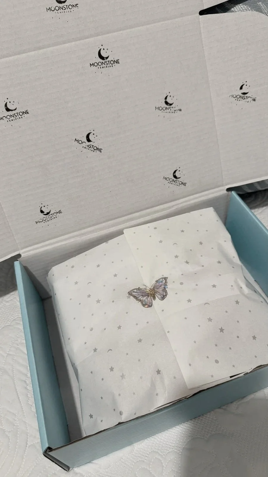 Open Moonstone Feminine box with tissue paper decorated with stars and a butterfly design inside.