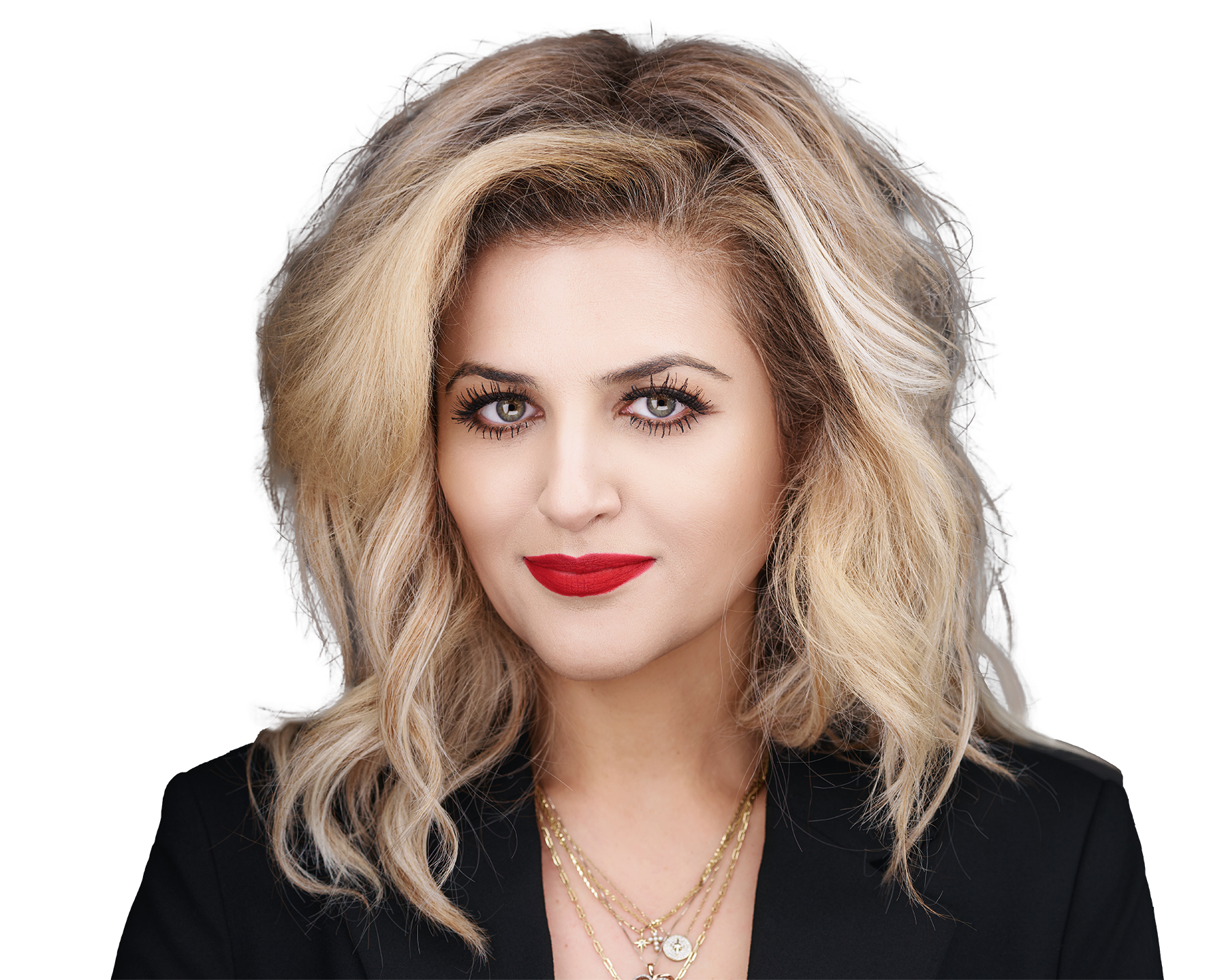 Close-up portrait of a woman with blonde, wavy hair and green eyes, wearing red lipstick, layered gold necklaces, and a black top against a black background.