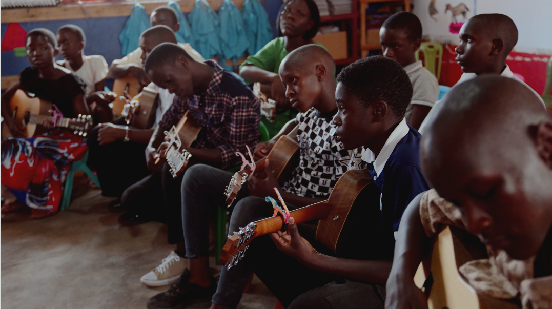 Group of children in a classroom playing guitars.