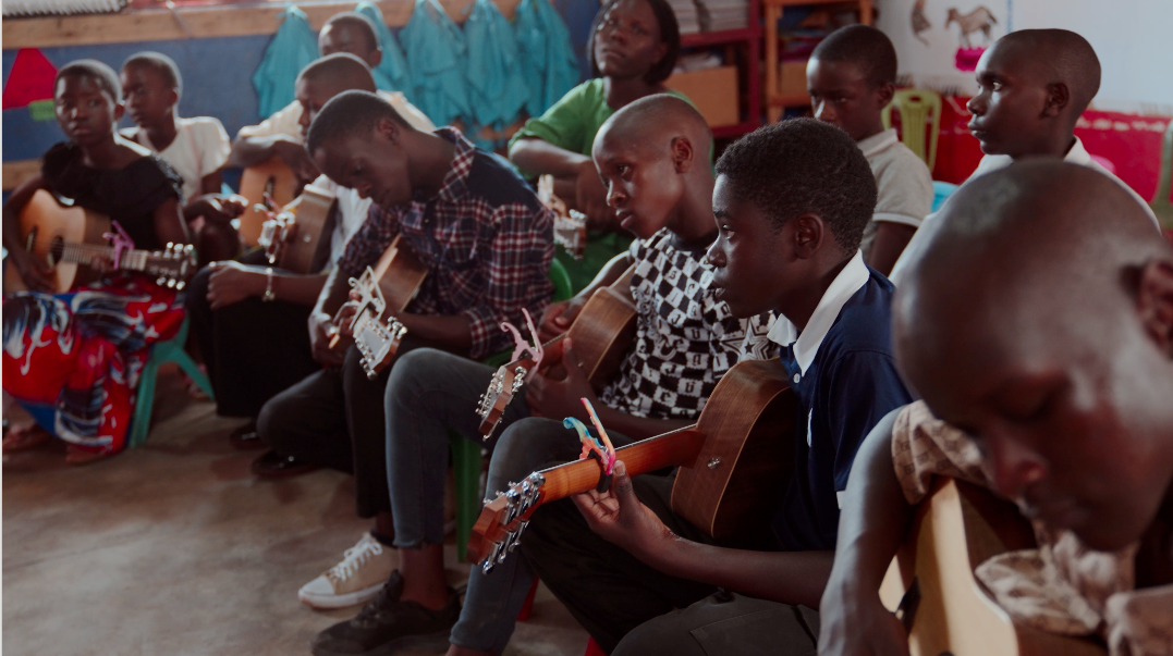 Group of children sitting together, playing guitars in a classroom.