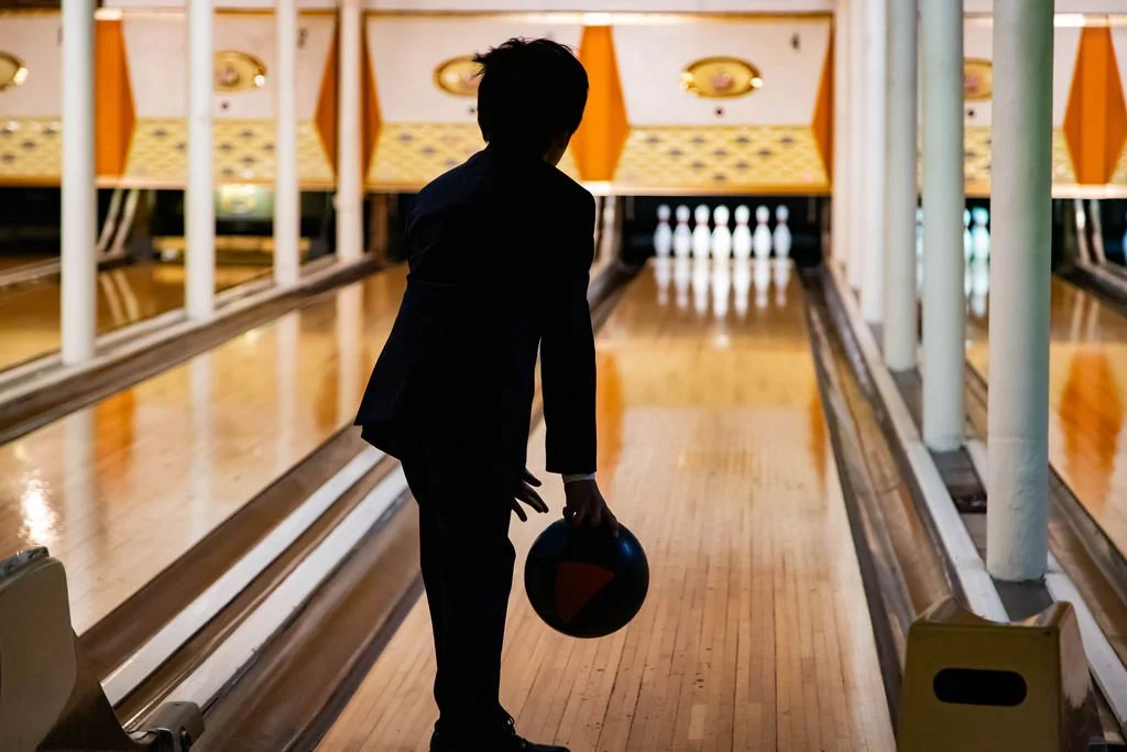 A person in a suit holding a bowling ball in a bowling alley, preparing to bowl.