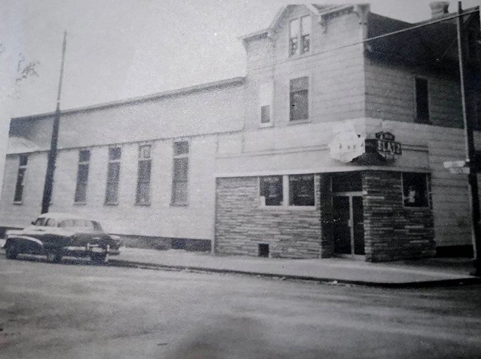Black and white photo of a two-story building on a city street with a car parked in front.